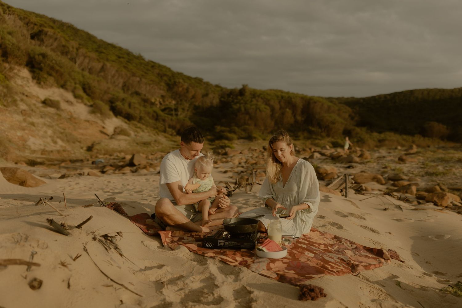 People enjoying a relaxed gathering on a rocky coastal beach at dusk.