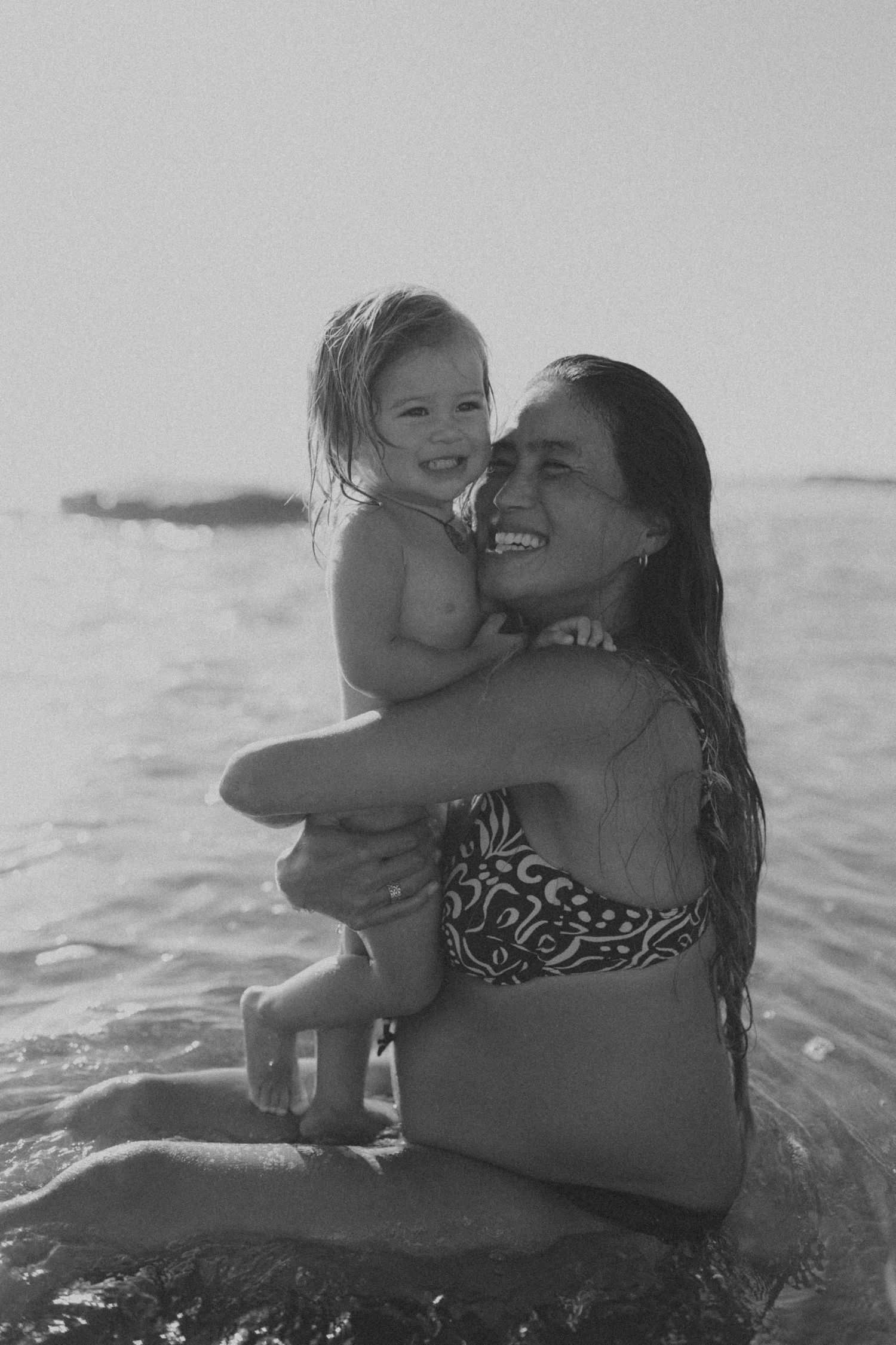 A parent and child share joyful moments while playing together in ocean waves during a sunny beach day.