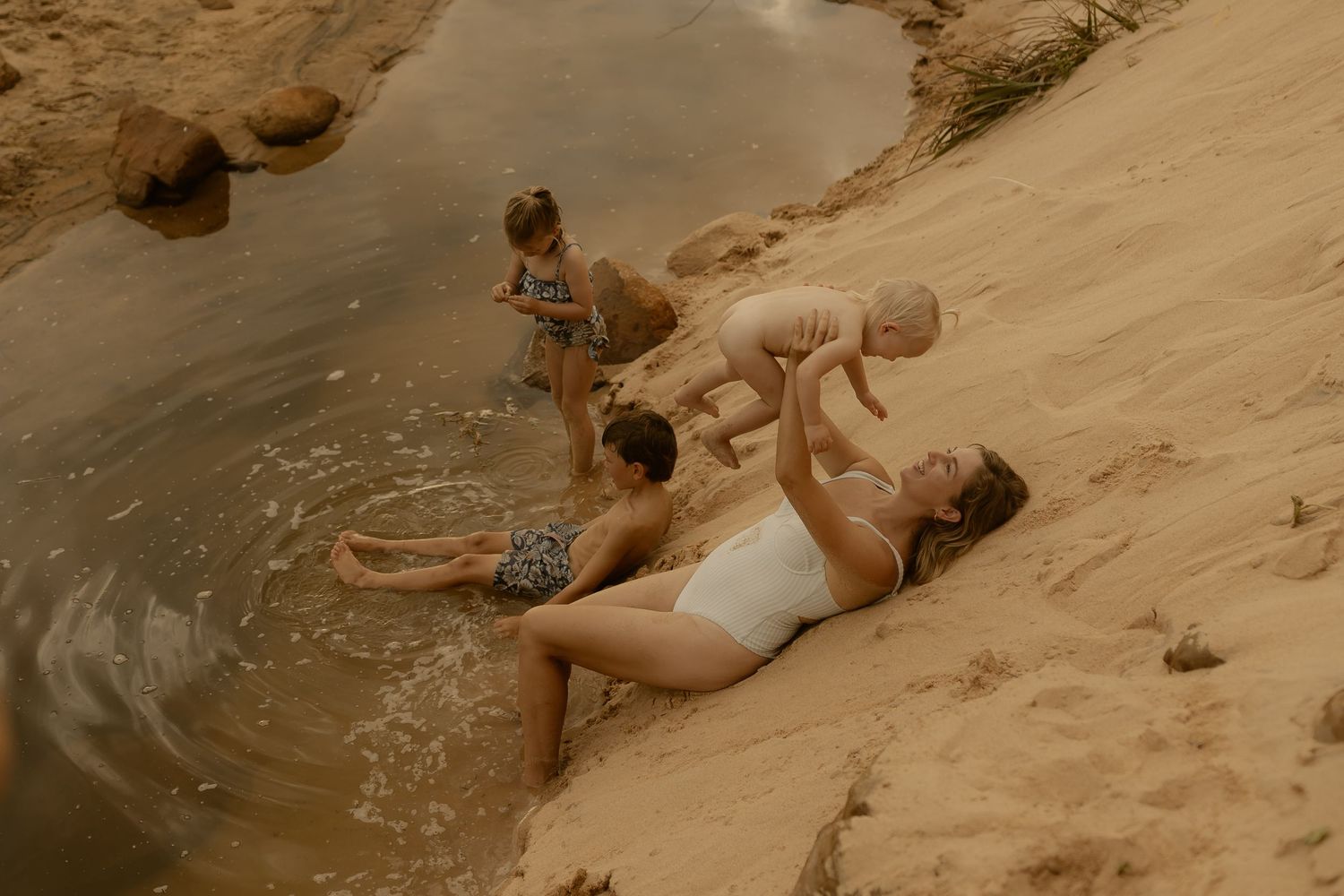A sequence of people sliding down a natural sandstone water slide into a refreshing pool on a sunny day.