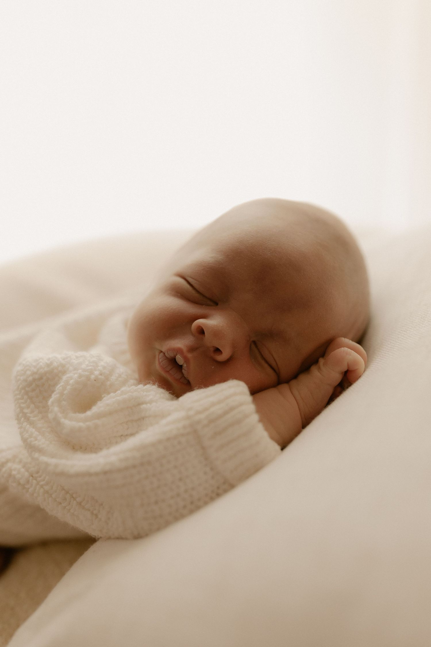 Peaceful sleeping newborn wrapped in white knit blanket captured in gentle sepia tones from different angles.