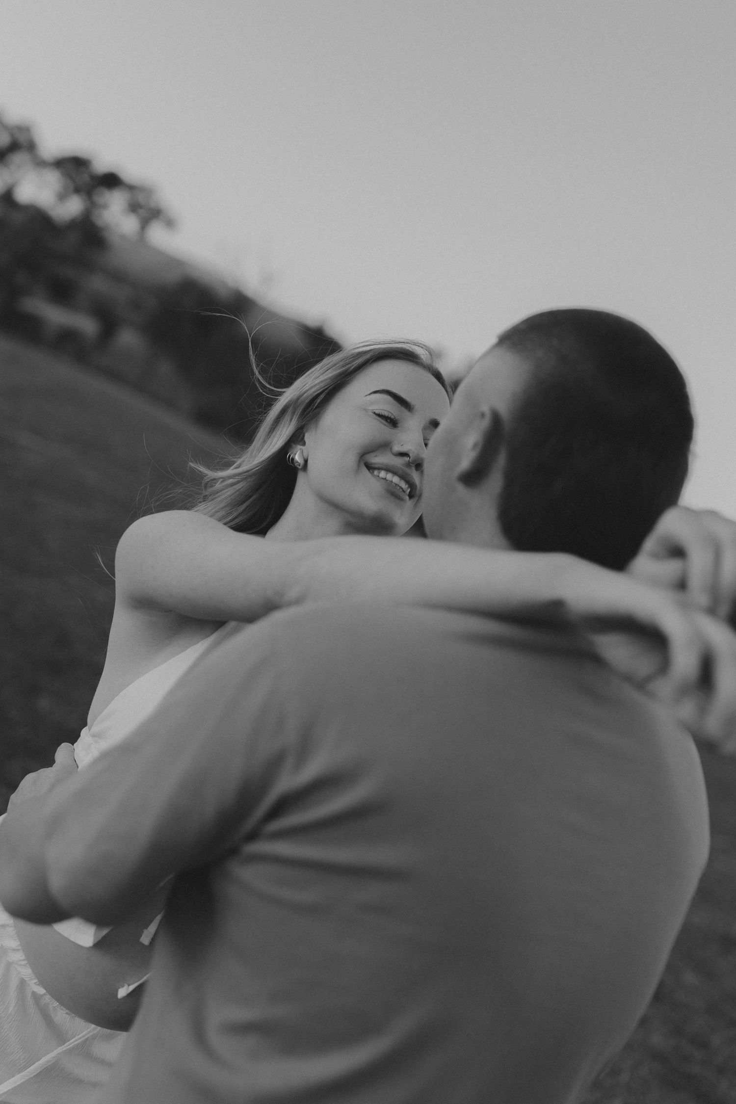 Black and white photo of smiling woman embracing partner in romantic outdoor setting.