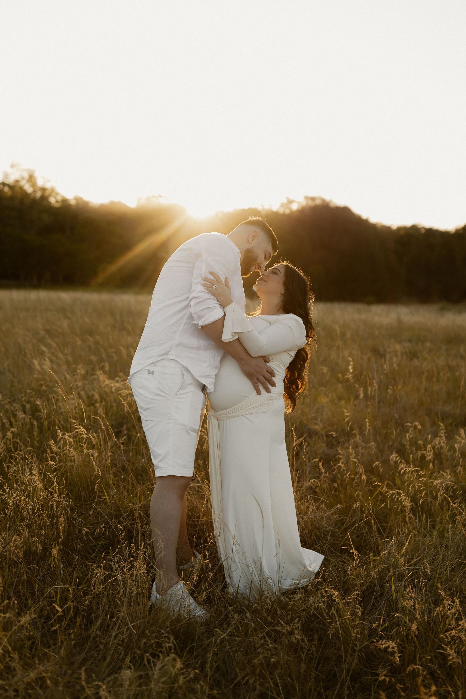 A romantic sunset moment captured in a golden field with two people in white outfits.
