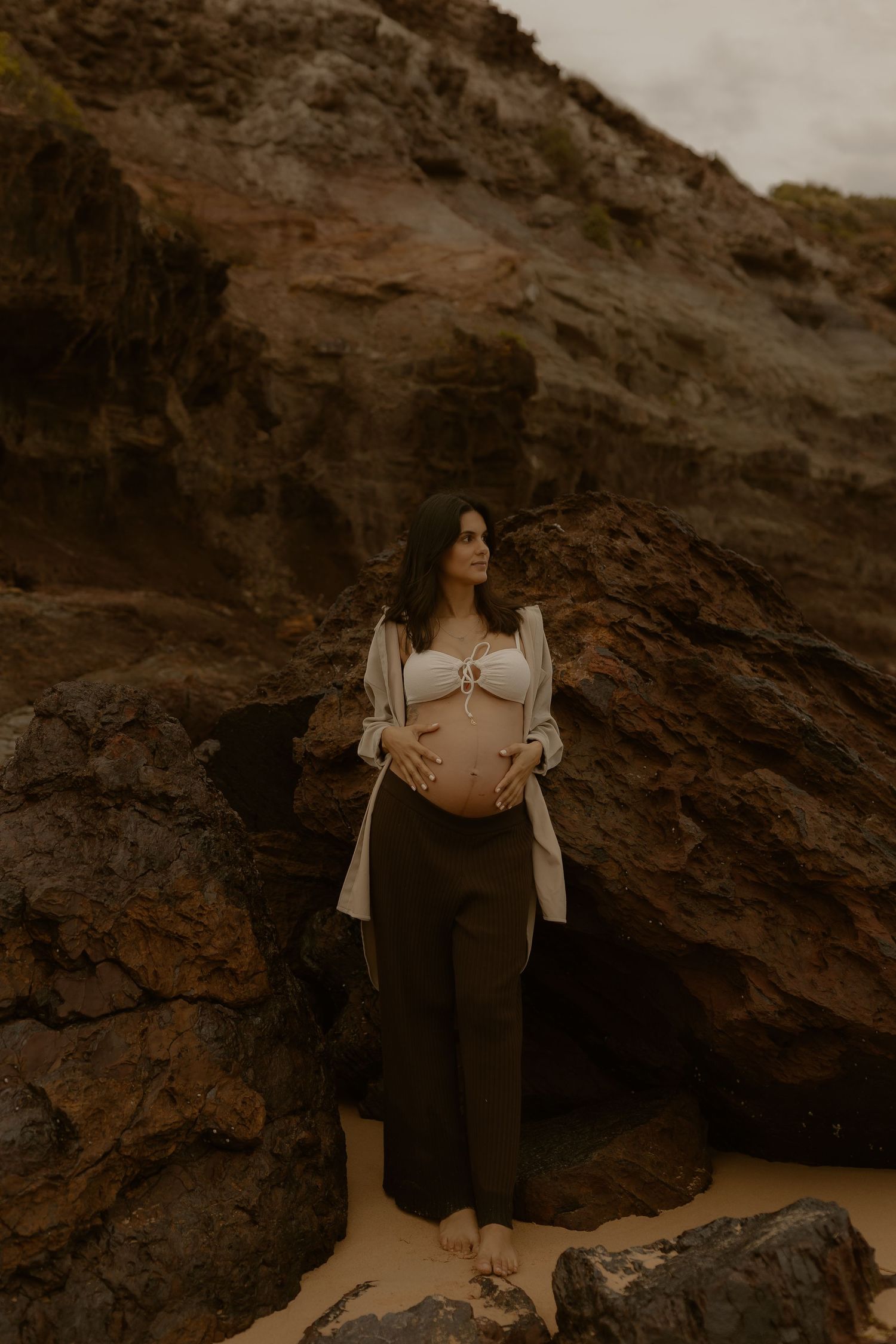 Maternity photoshoot against dramatic rocky cliffs in warm earth tones at sunset.