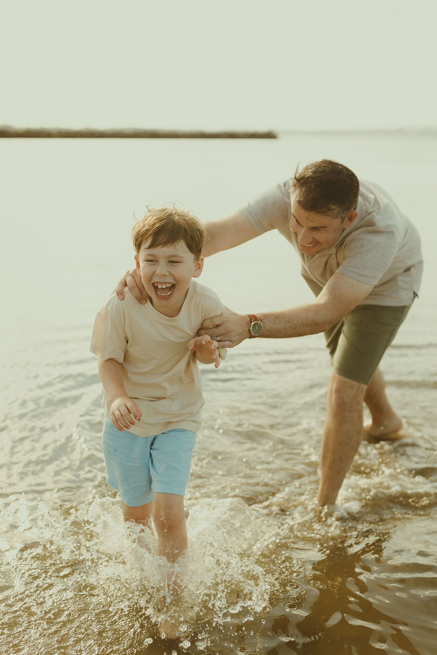 A joyful moment at the beach as a parent and child play in the splashing waves during golden hour.