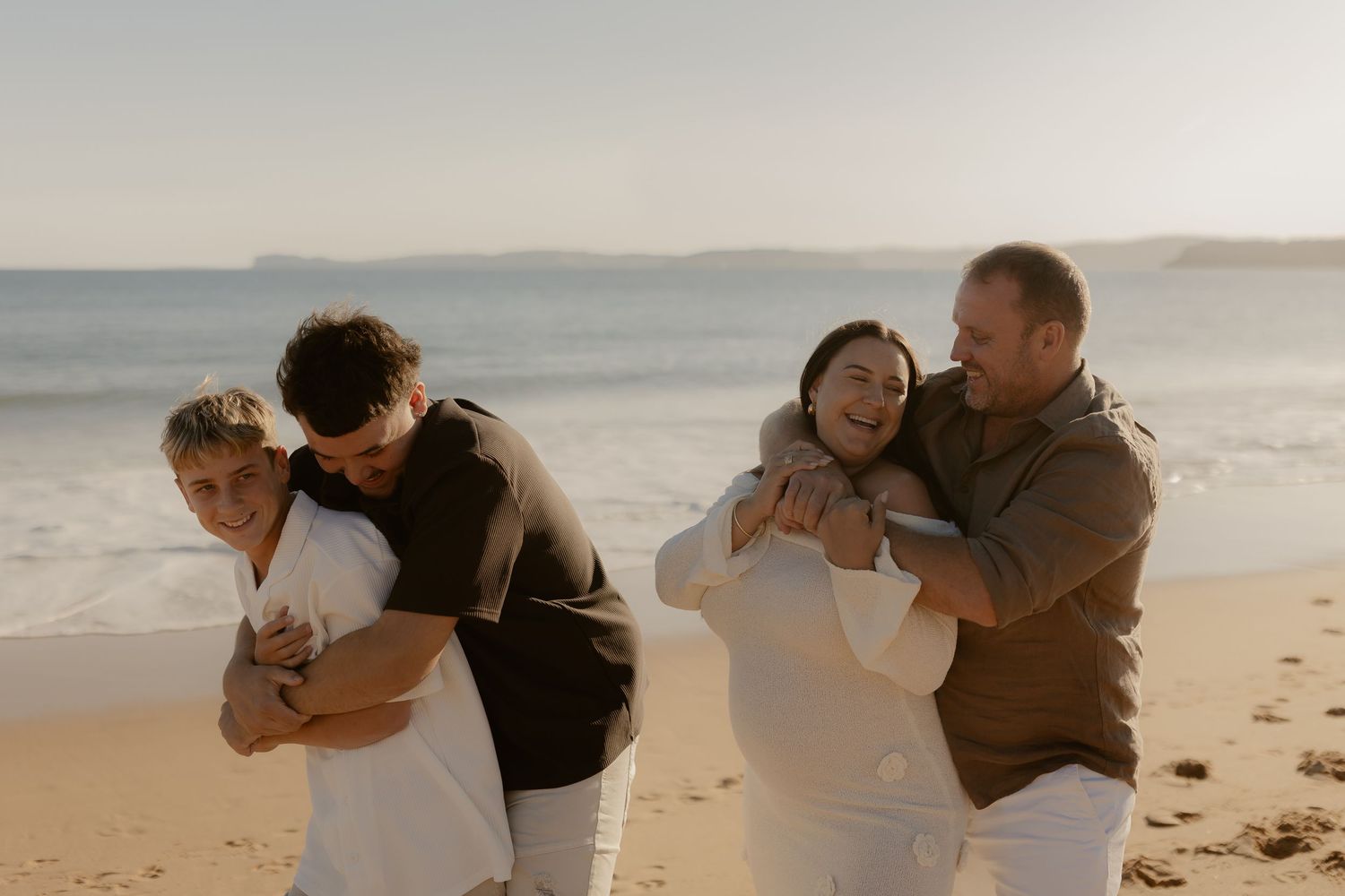 A couple embraces lovingly on a sunny beach during sunset.