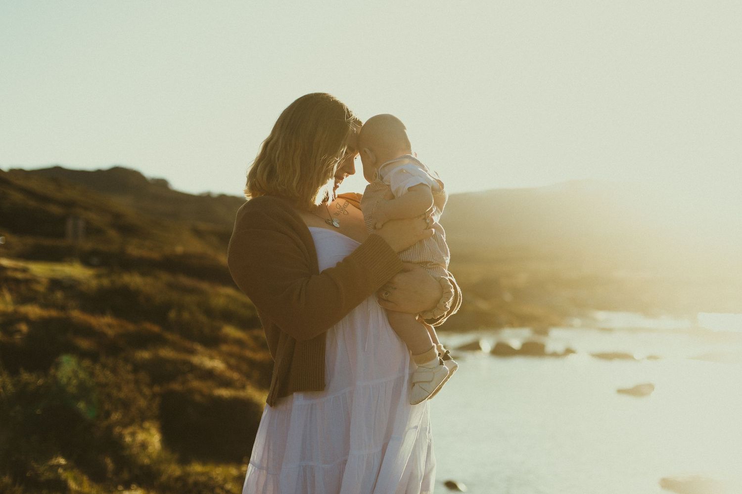 Silhouette of figures embracing on a coastal cliff at golden hour with sunlight streaming through the scene.