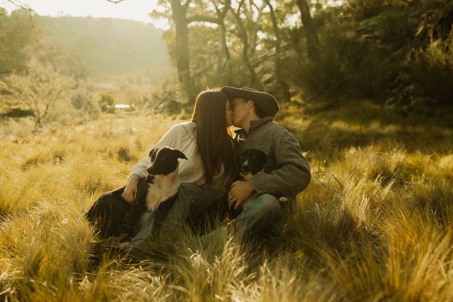 A couple shares an intimate moment while sitting together in a sunlit field of golden grass at sunset.