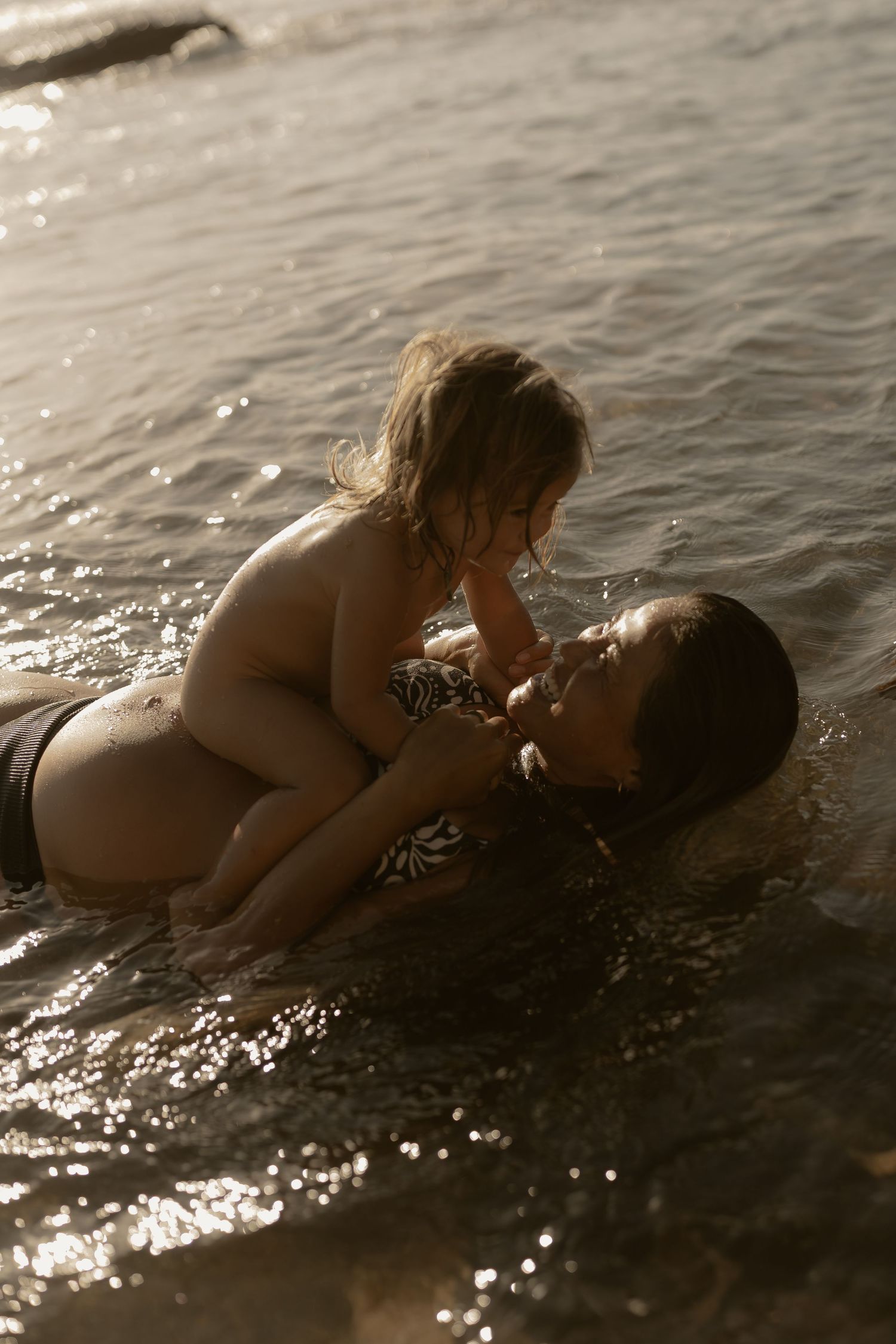 A tender moment of play and connection in sparkling water at sunset.