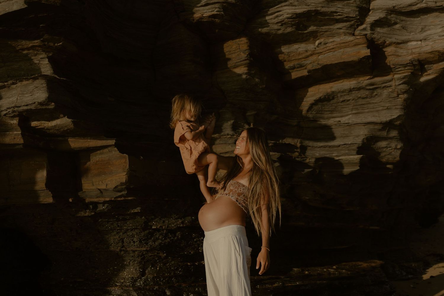 Romantic seaside moment captured between two people on a dramatic beach with rocky cliffs at dusk.