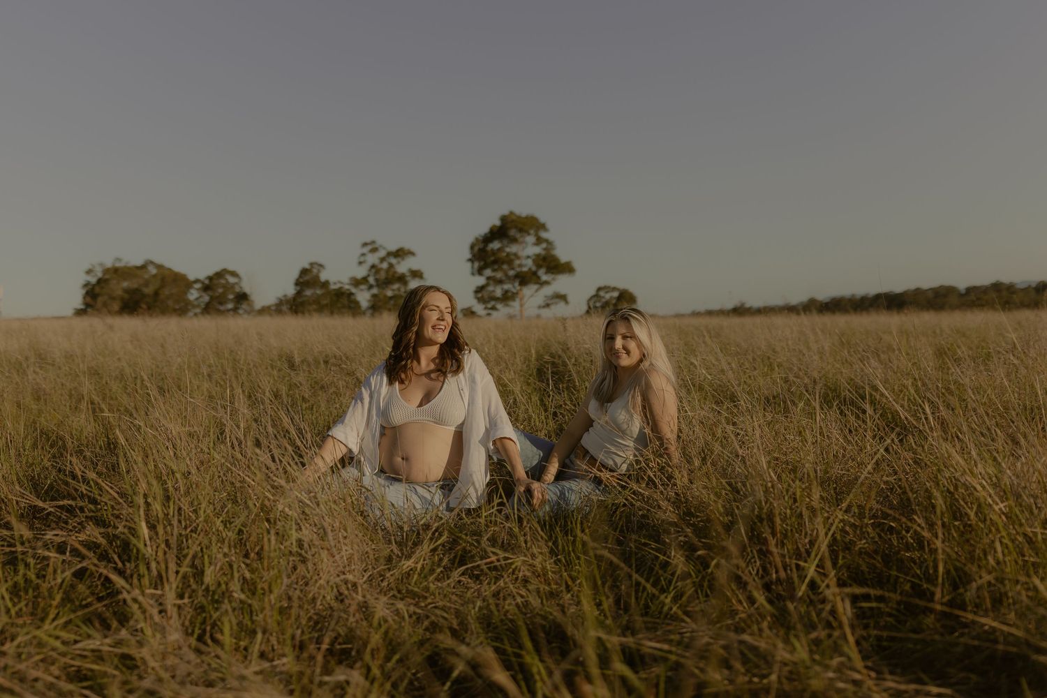 Friends laugh together while sitting in a golden wheat field during sunset.