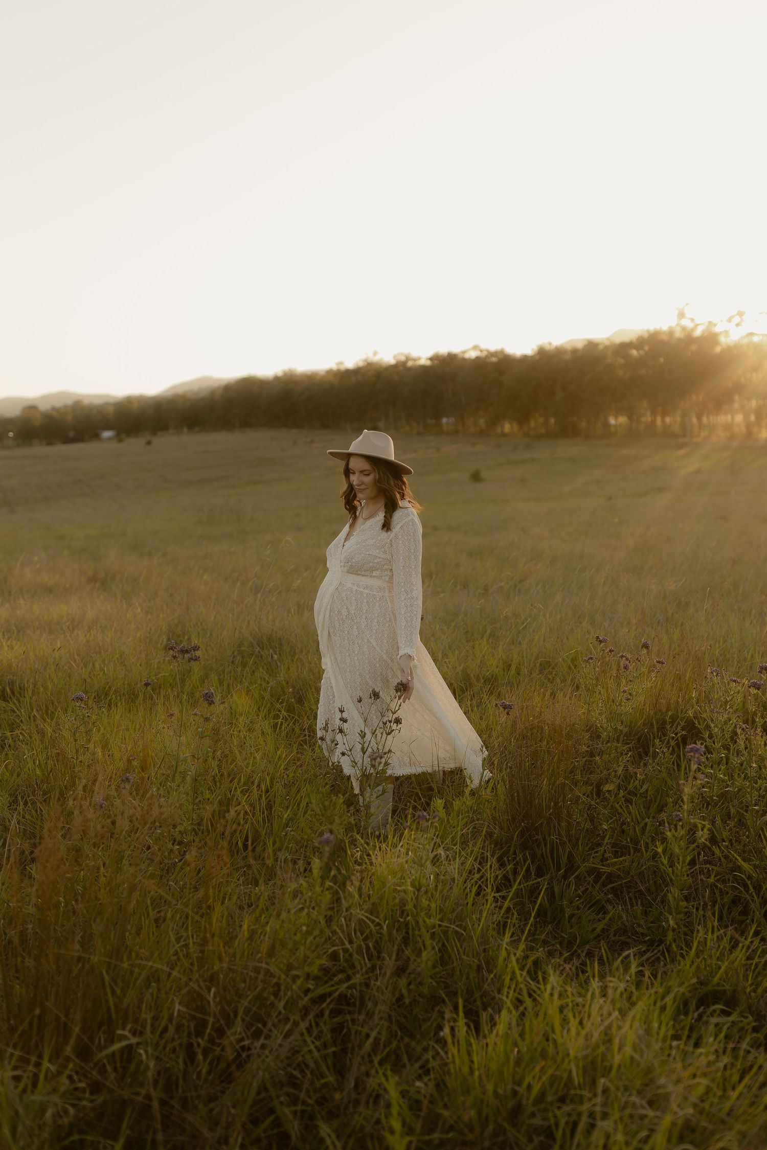A dreamy sunset scene captures someone in white walking through a wild meadow with tall grasses.