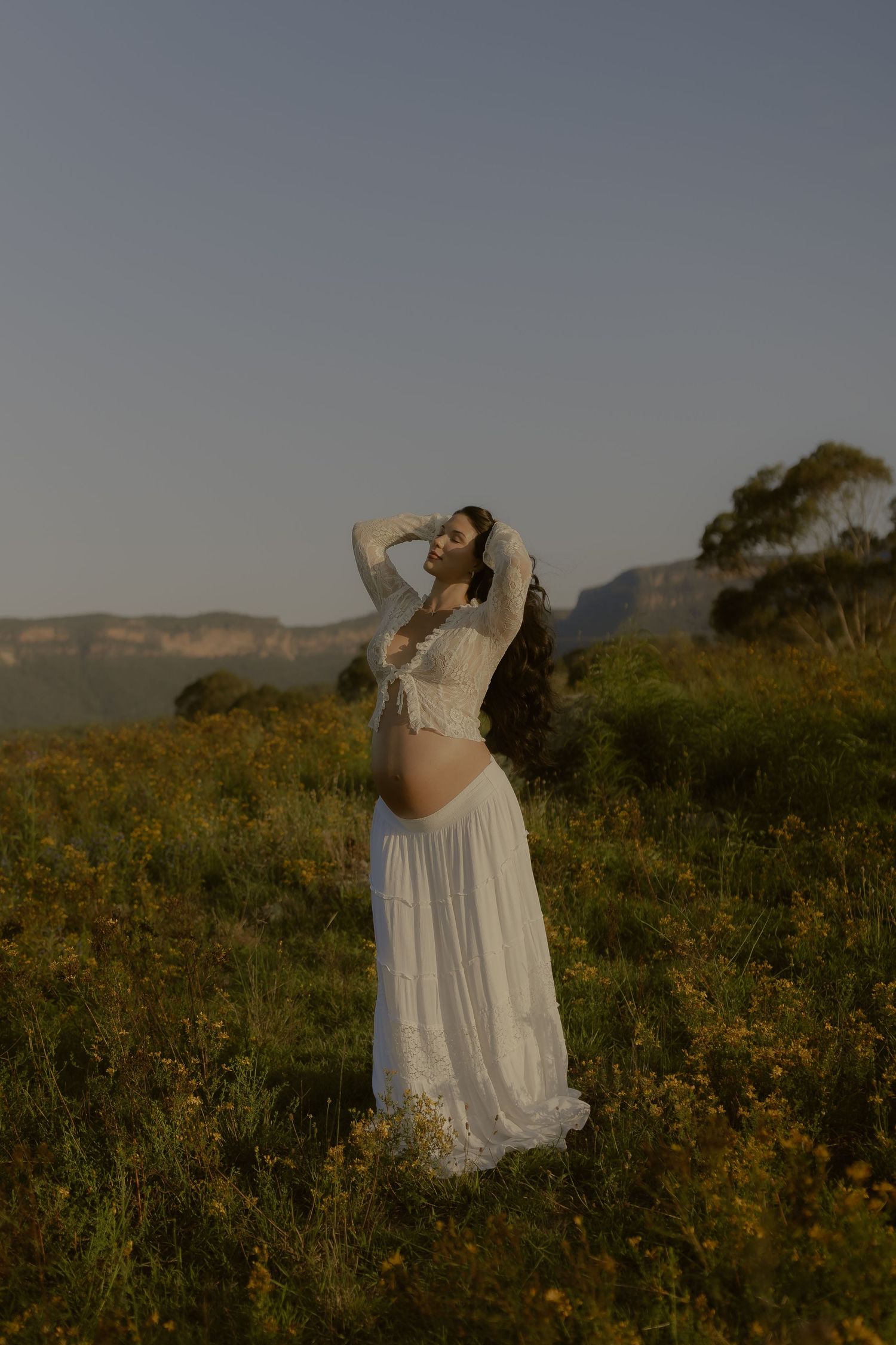A white flowy dress twirls gracefully in a golden wildflower field at sunset.