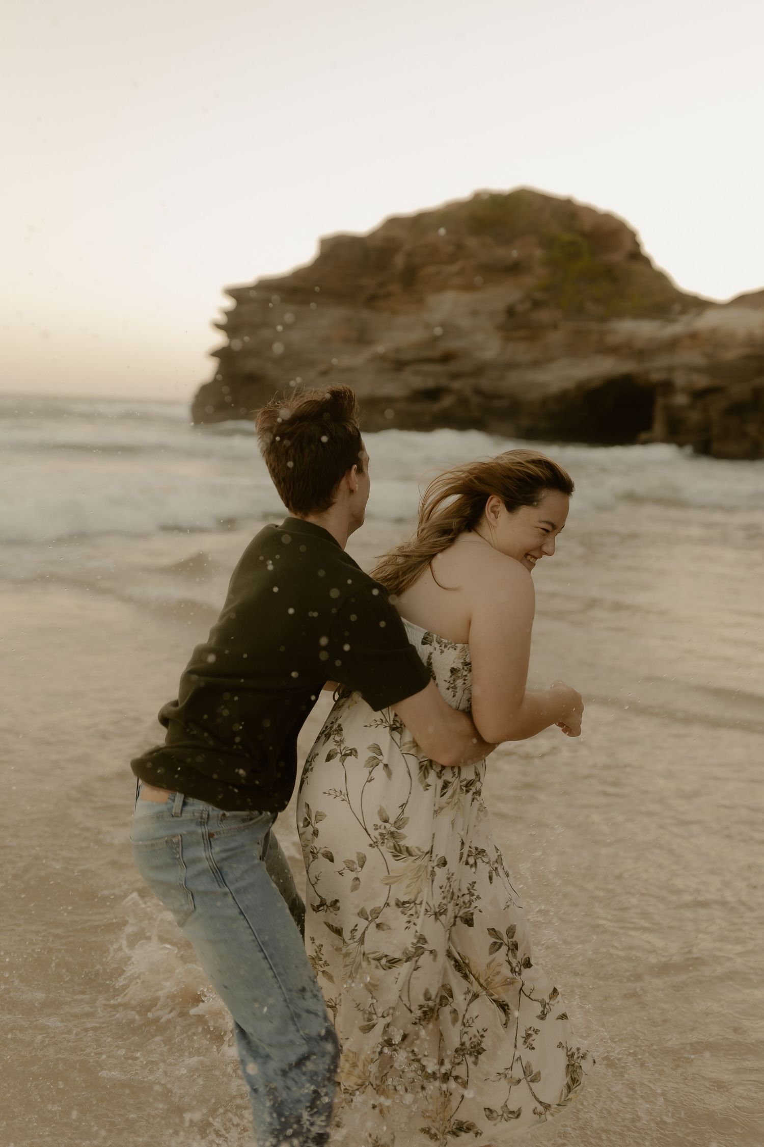 Two people running and playing together on a beach near rocky cliffs.