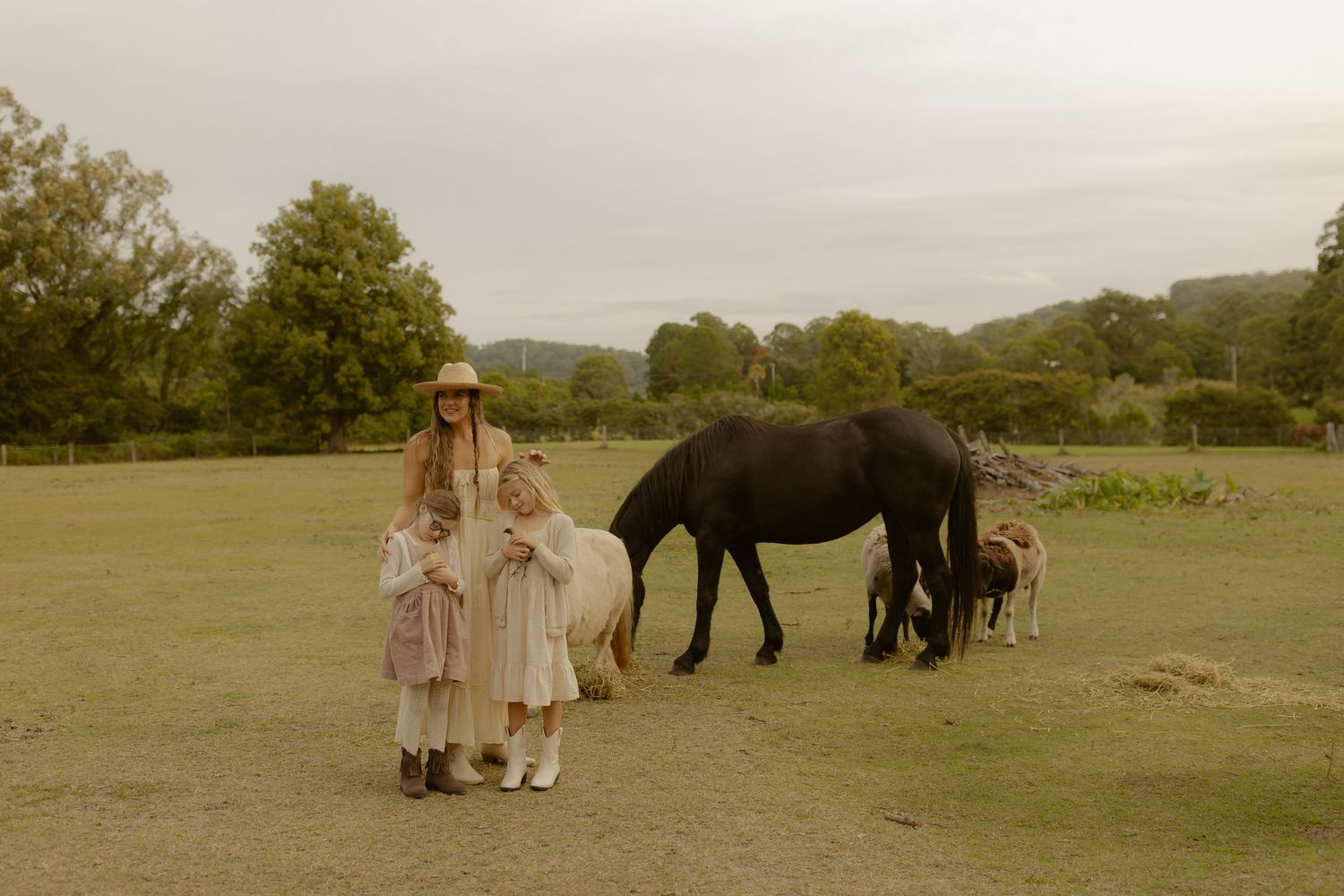 A woman and two young children stand with a white pony and black horse in an open field.