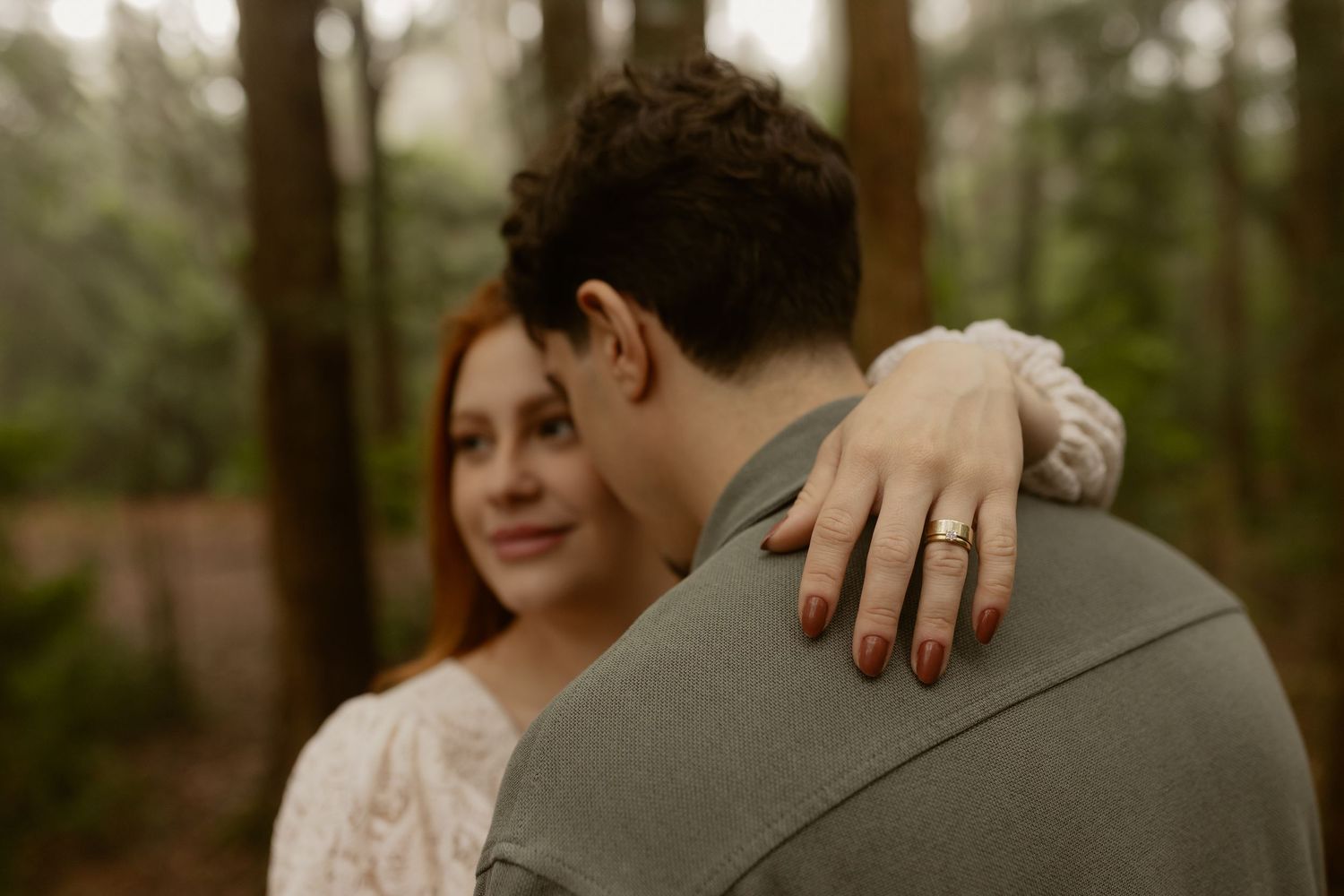Close-up shot of hands holding a lace wedding dress in a forest setting.