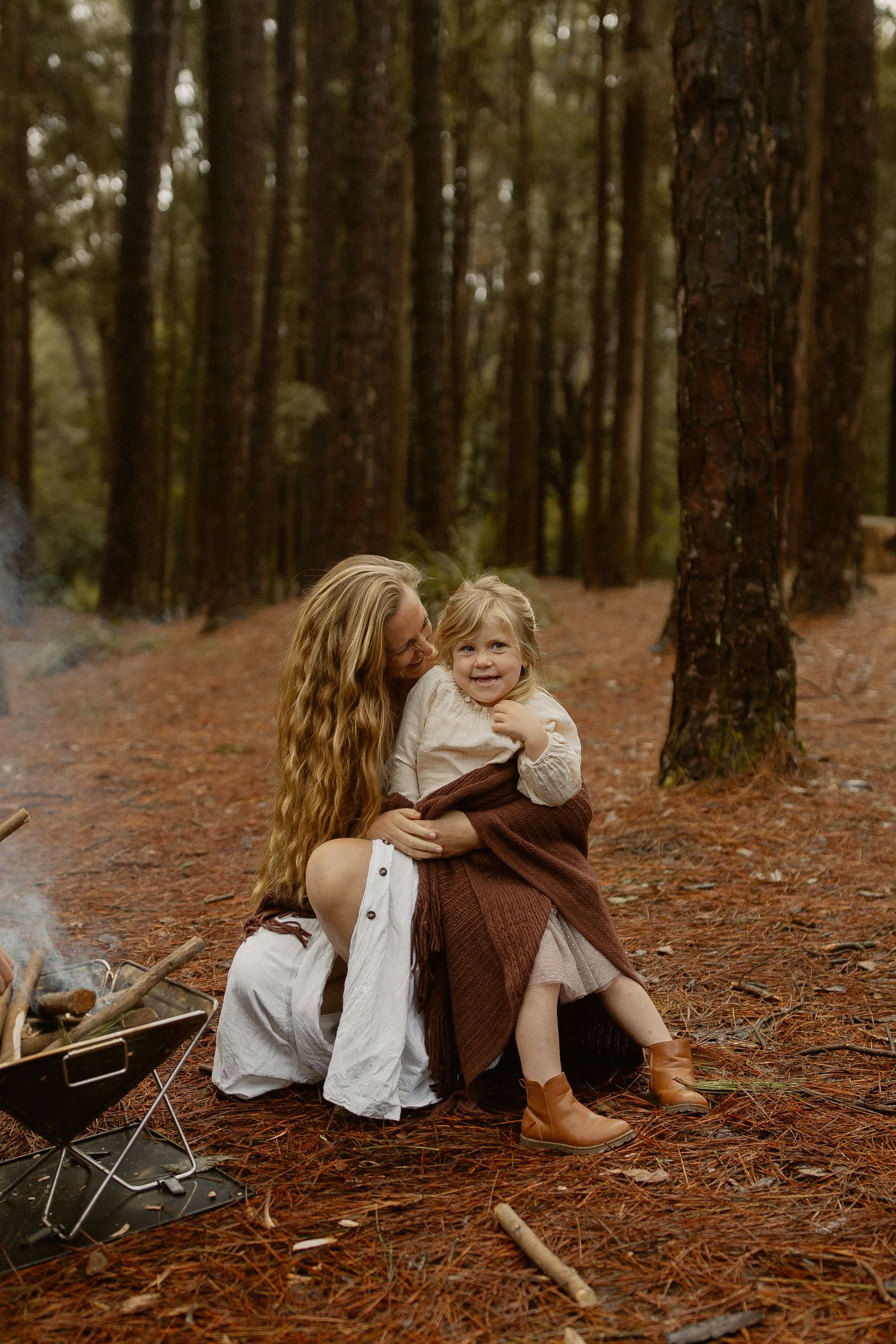 A whimsical woodland scene with vintage-styled figures sitting on fallen pine needles in a forest setting.
