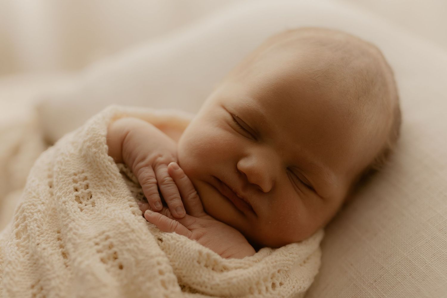 Close up view of tiny newborn baby feet wrapped in soft beige knit blanket.