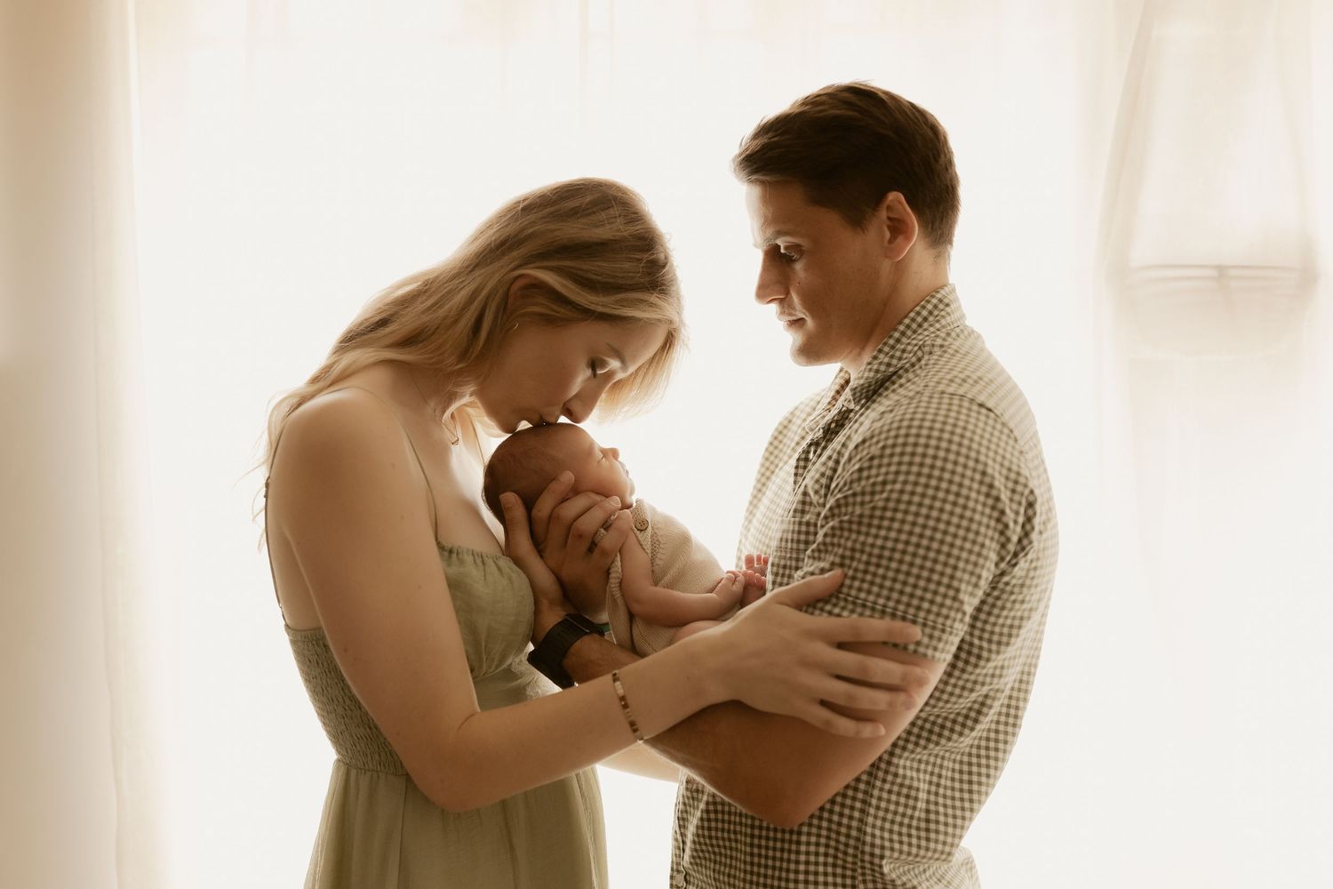 Family portrait with new parents cradling their infant in gentle natural light.