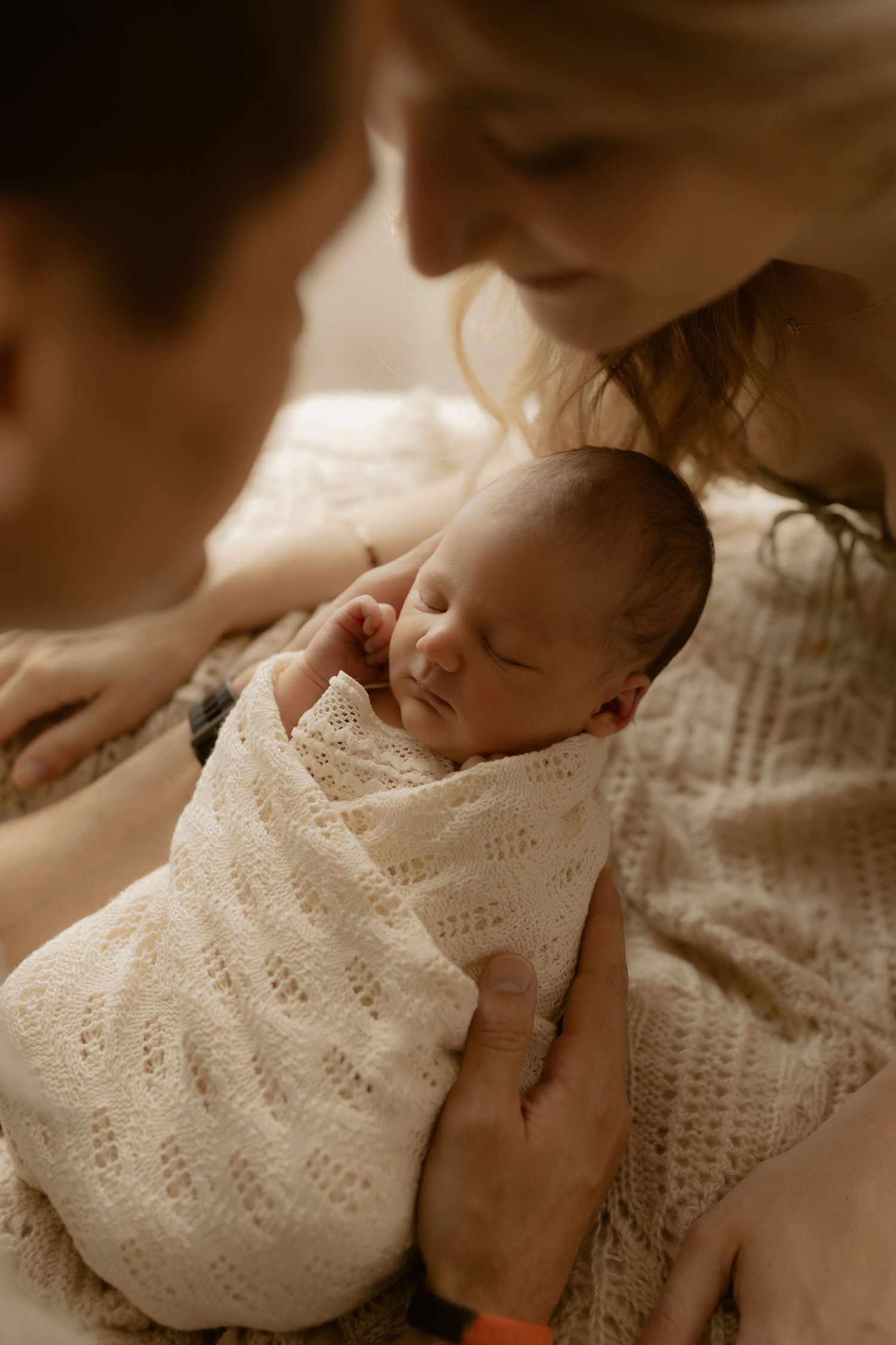 Newborn swaddled in delicate white lace blanket in warm sepia tones.