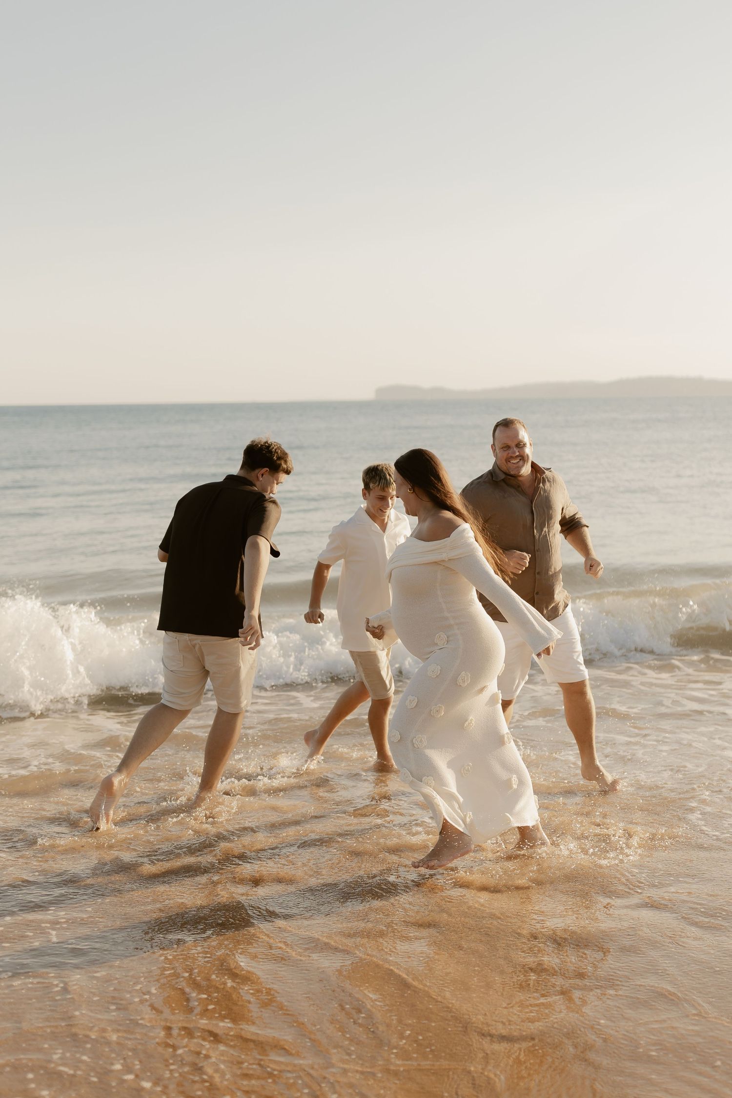 A group plays and splashes together in the ocean waves at sunset.