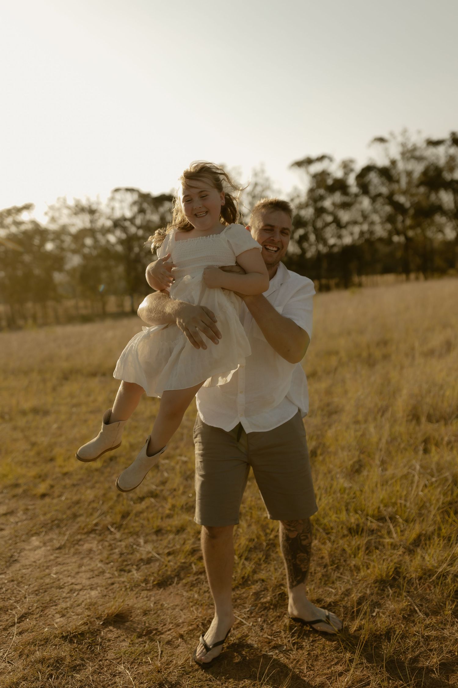 A couple dances playfully together in a sunlit meadow at golden hour.