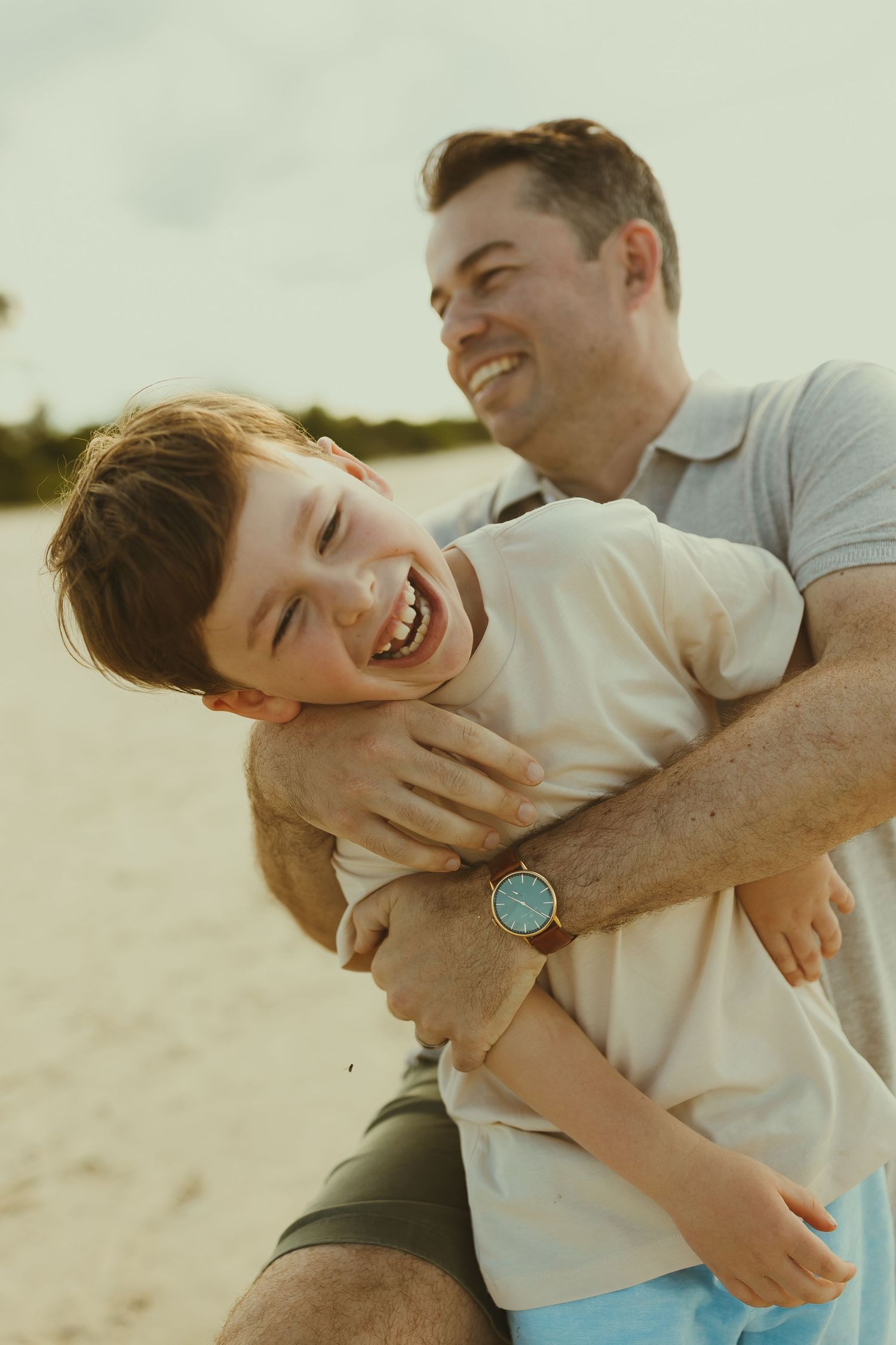 A playful moment between parent and child sharing laughter and embraces on a sunny beach.