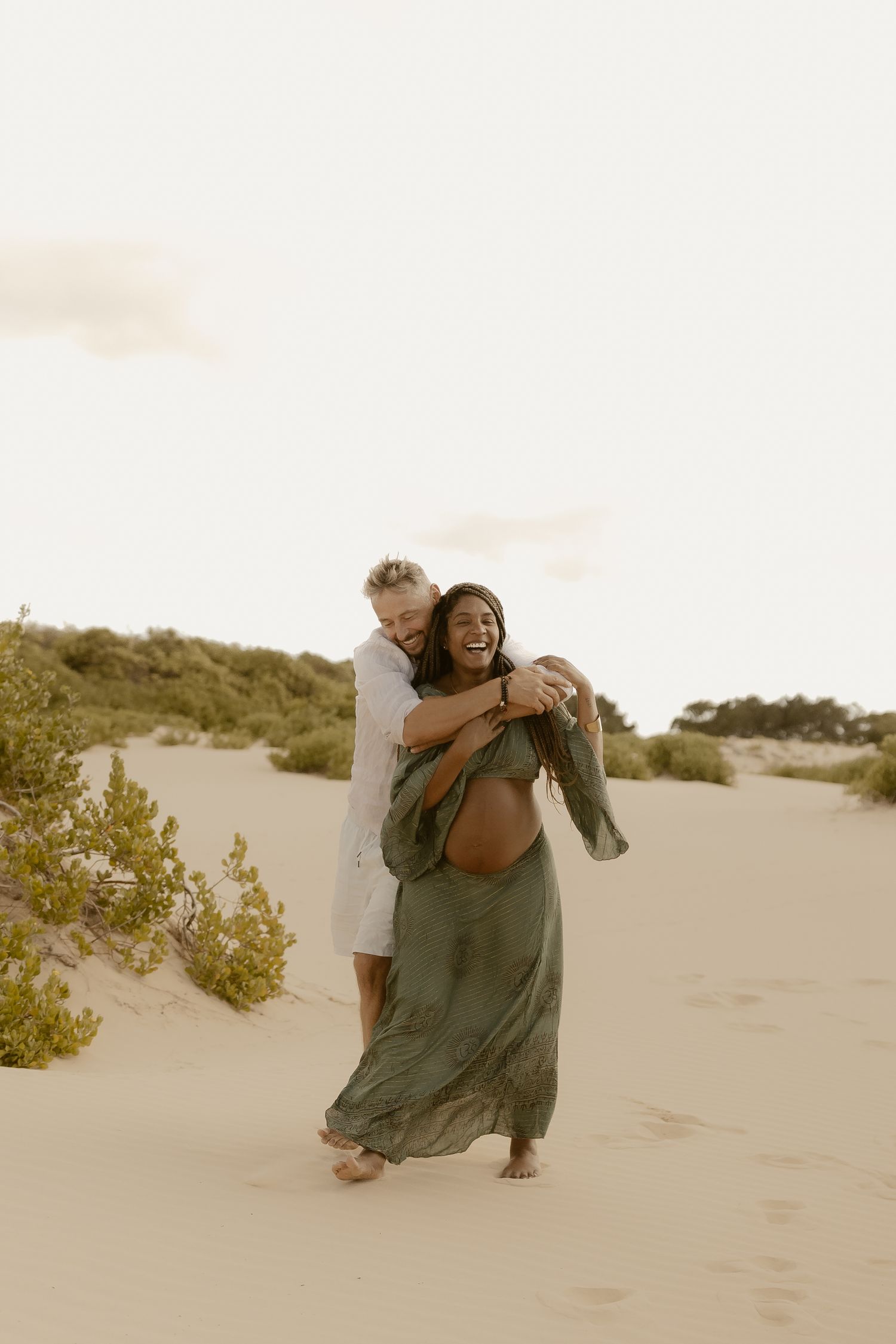 Two people share intimate moments while posing together on desert sand dunes.