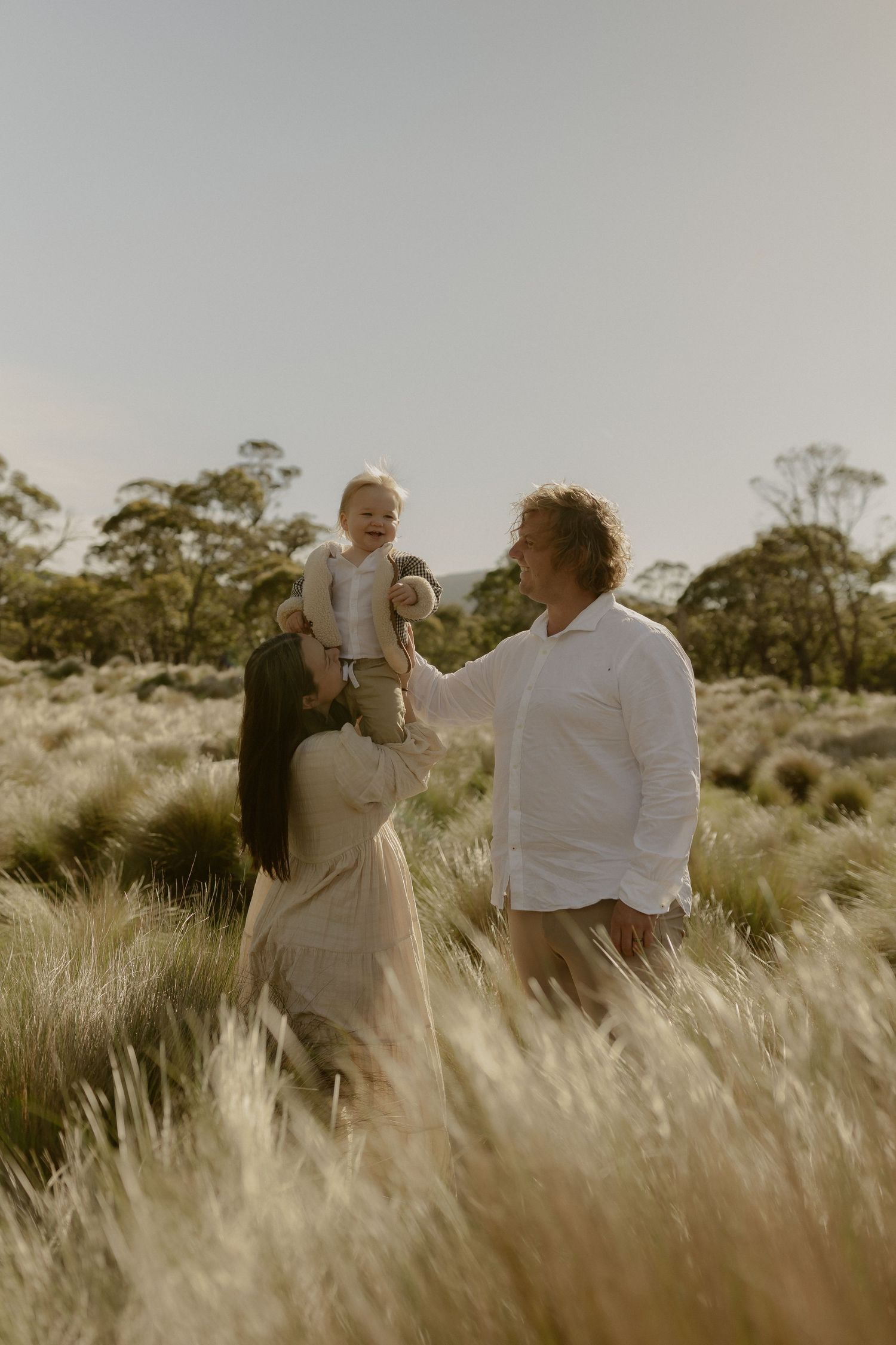 A joyful family moment captured in a sun-lit field of tall grass during golden hour.