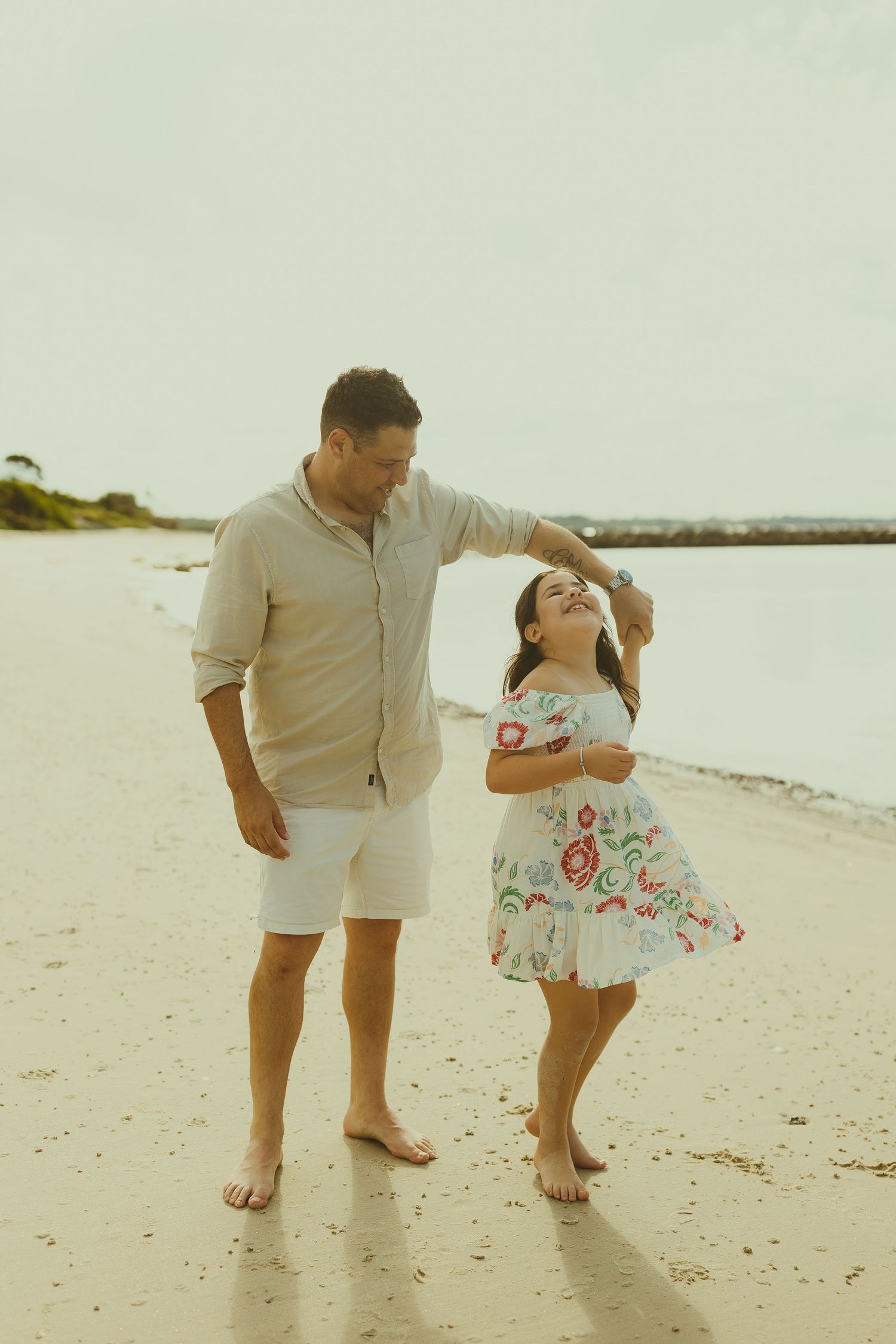 A couple playfully walking and dancing together barefoot on a serene beach at sunset.