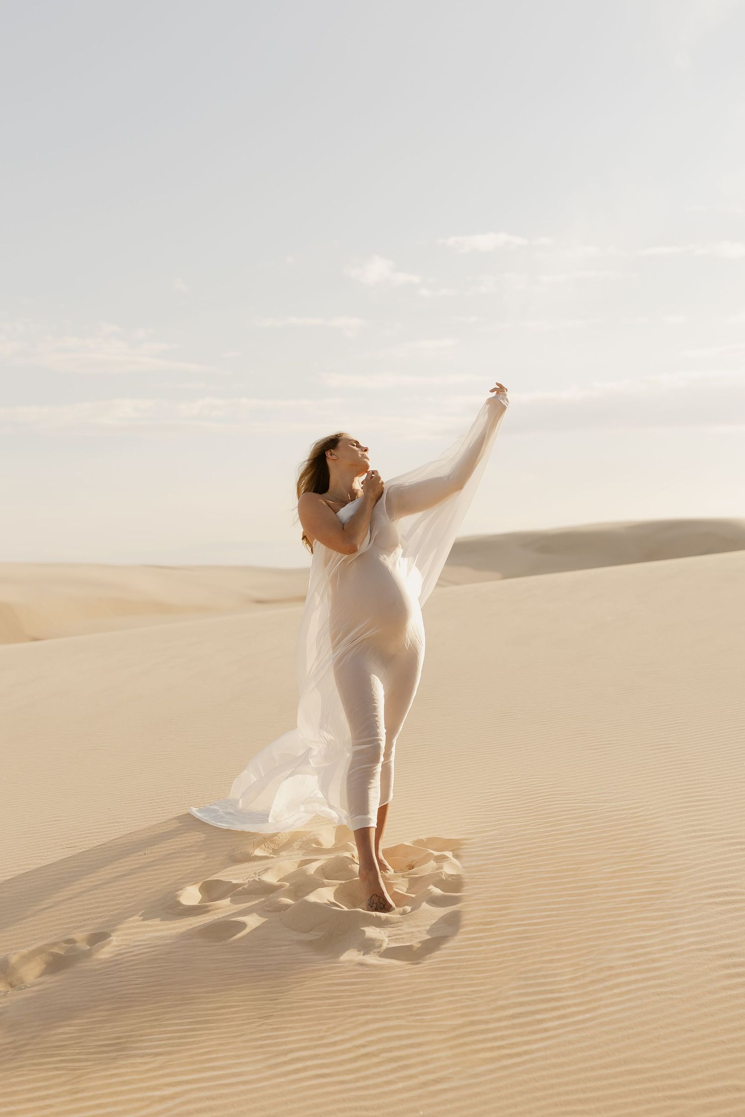 Ethereal desert photography with flowing white fabric caught in the breeze against sand dunes.
