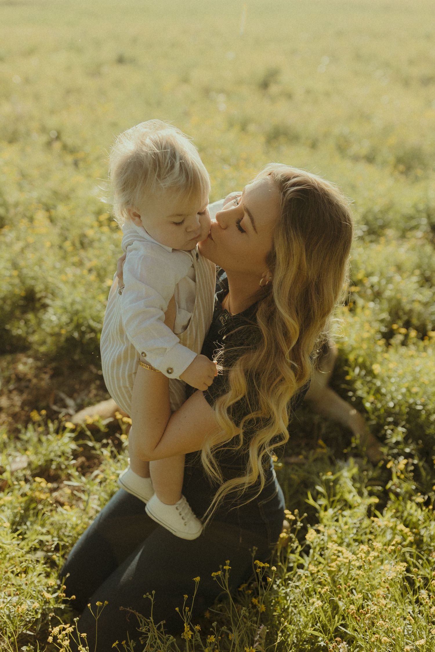 Tender family moment captured in golden sunlight while sitting in a grassy meadow.