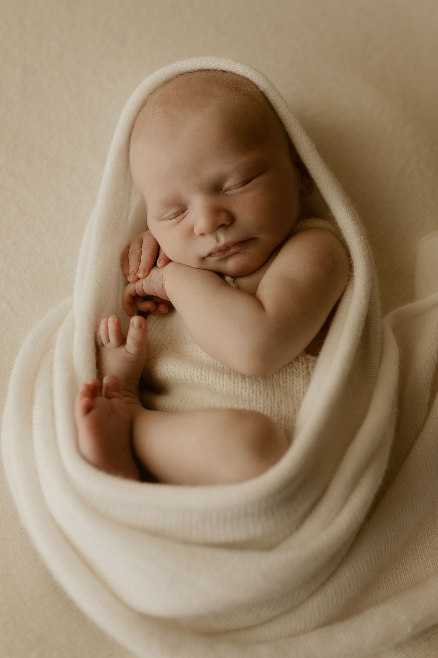 Series of sepia-toned photographs showing peaceful sleeping baby swaddled in soft white blanket.