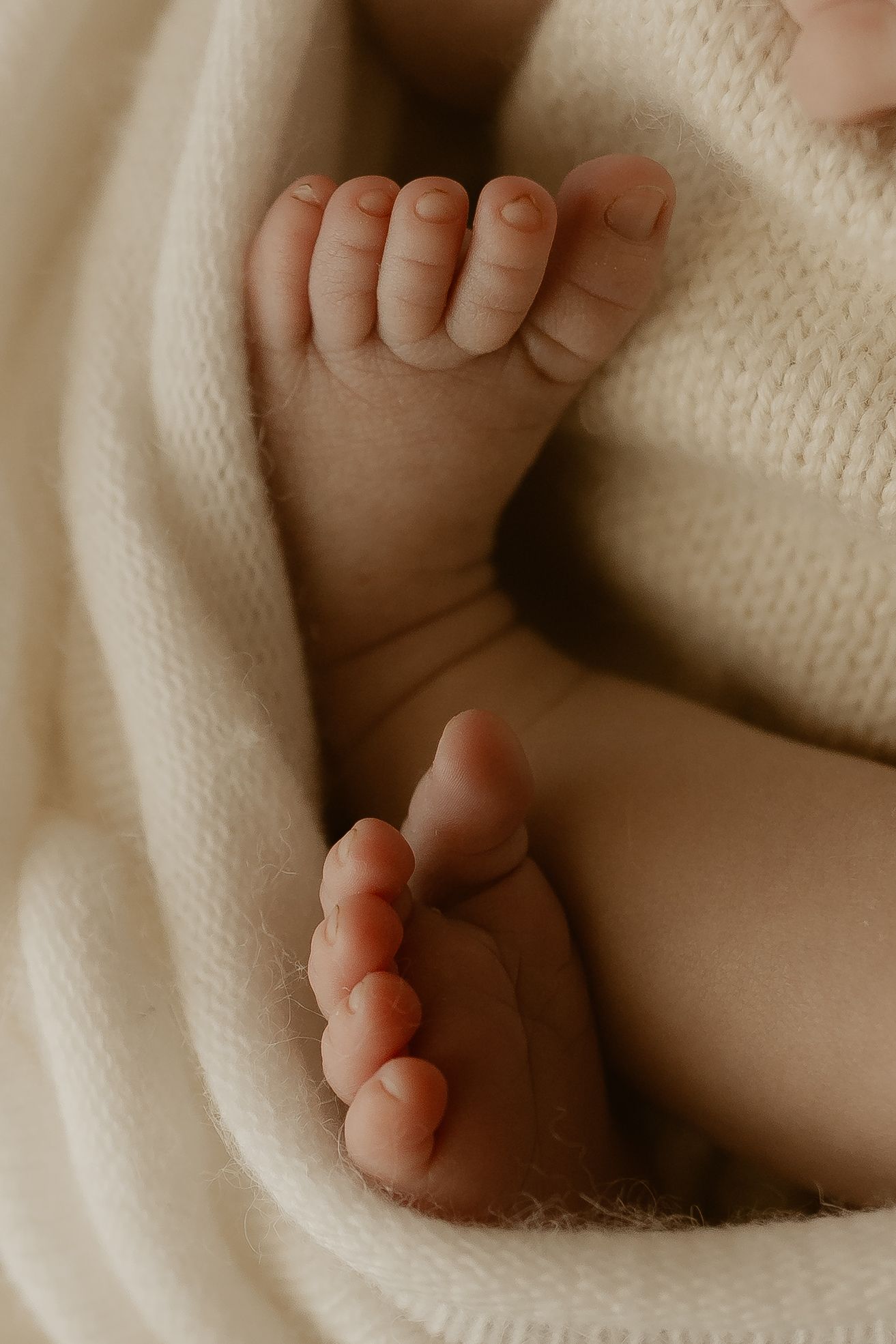 Tiny newborn baby toes wrapped in soft white knitted blanket shown in close up detail.