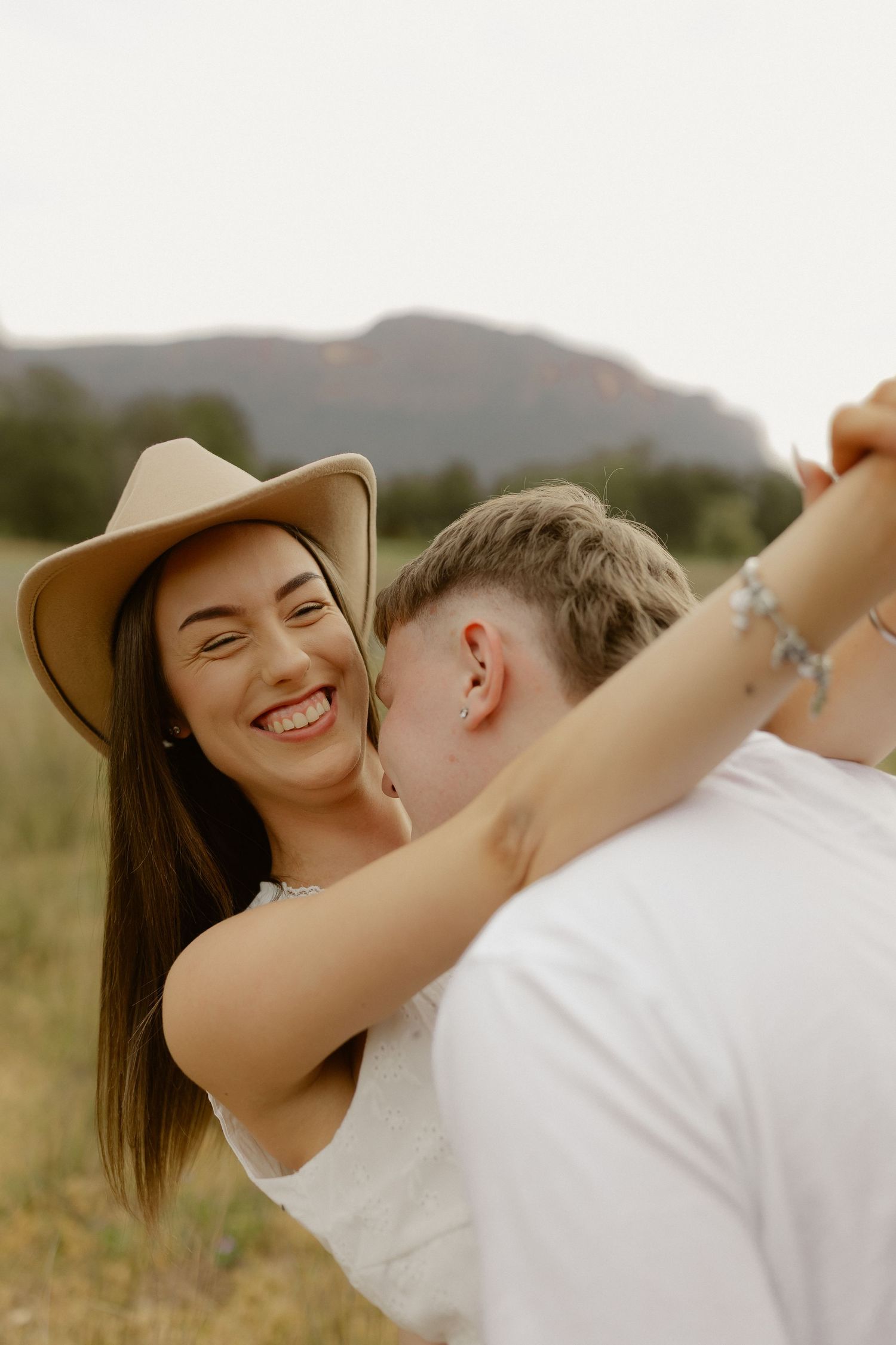 A romantic couple shares intimate moments against a scenic mountain backdrop at sunset.