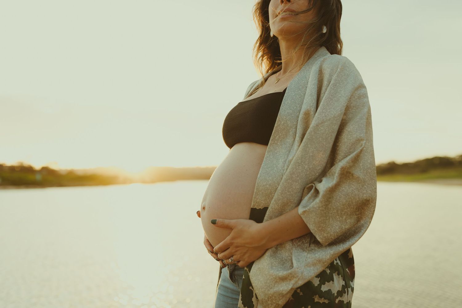 A maternity photo session at sunset shows a couple embracing on a sandy beach.