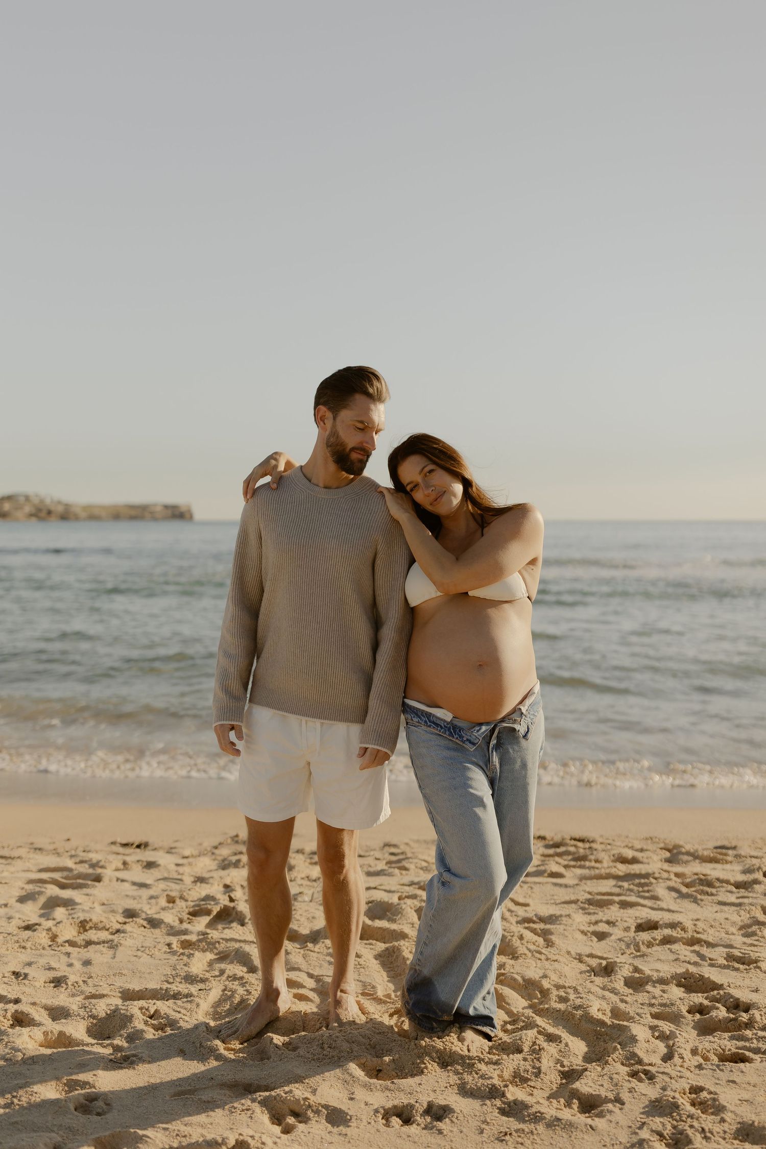 Couple walking together on sandy beach at sunset wearing casual attire.