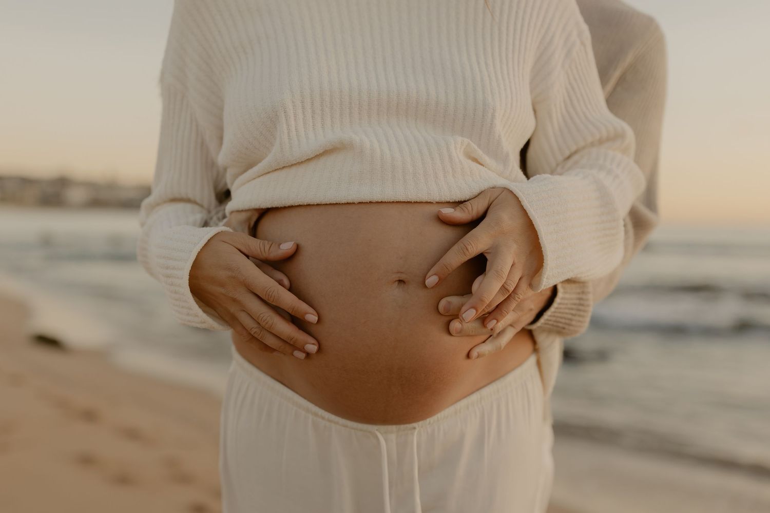 A series of cropped maternity photos showing a pregnant belly in a cream sweater against a warm sunset background.