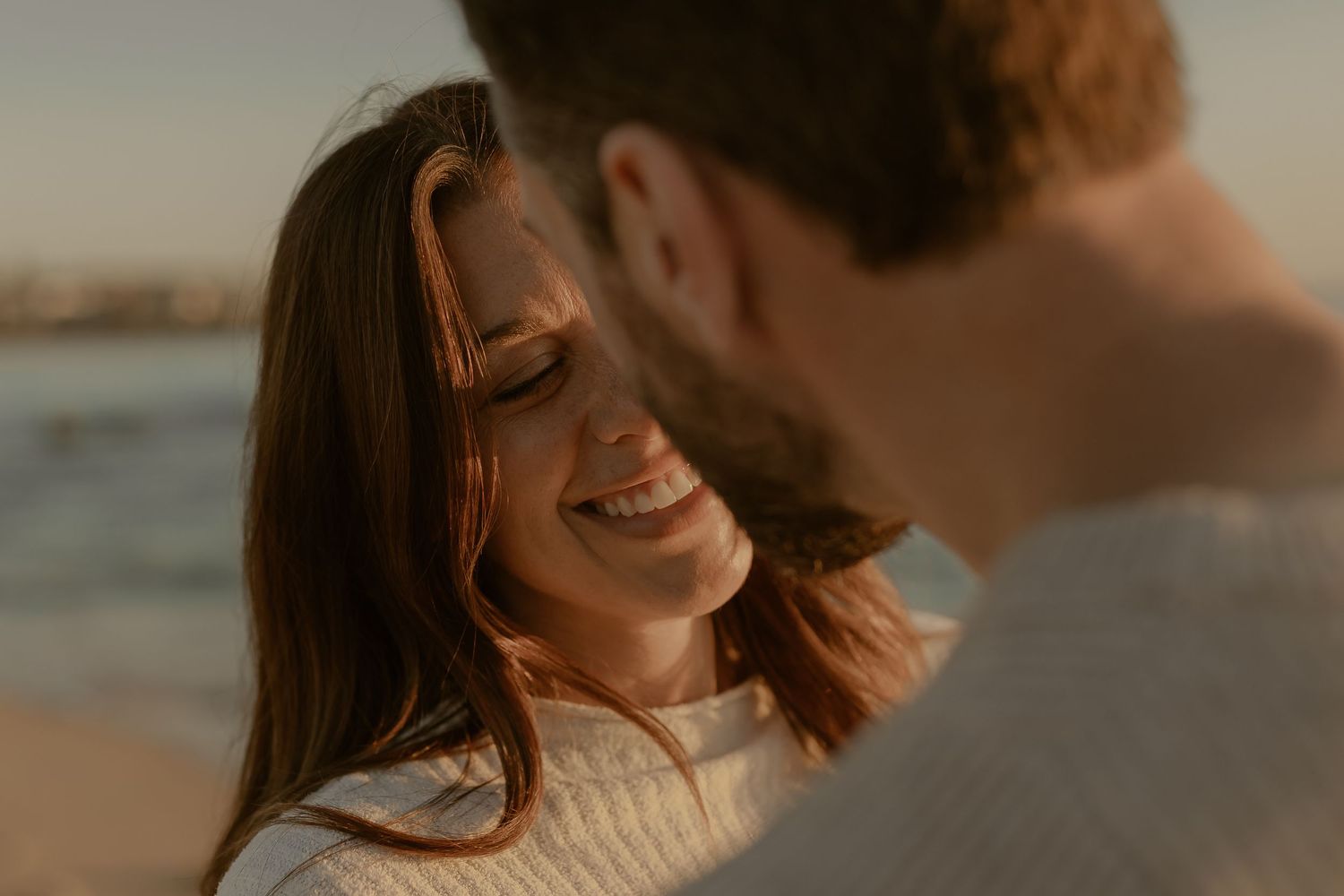 Romantic couple embraces on beach at sunset with golden light illuminating their silhouettes.