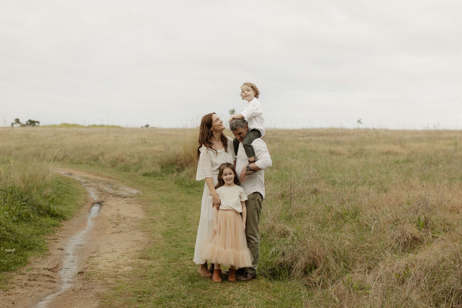 A group poses together on a dirt path through tall grass during an outdoor portrait session.