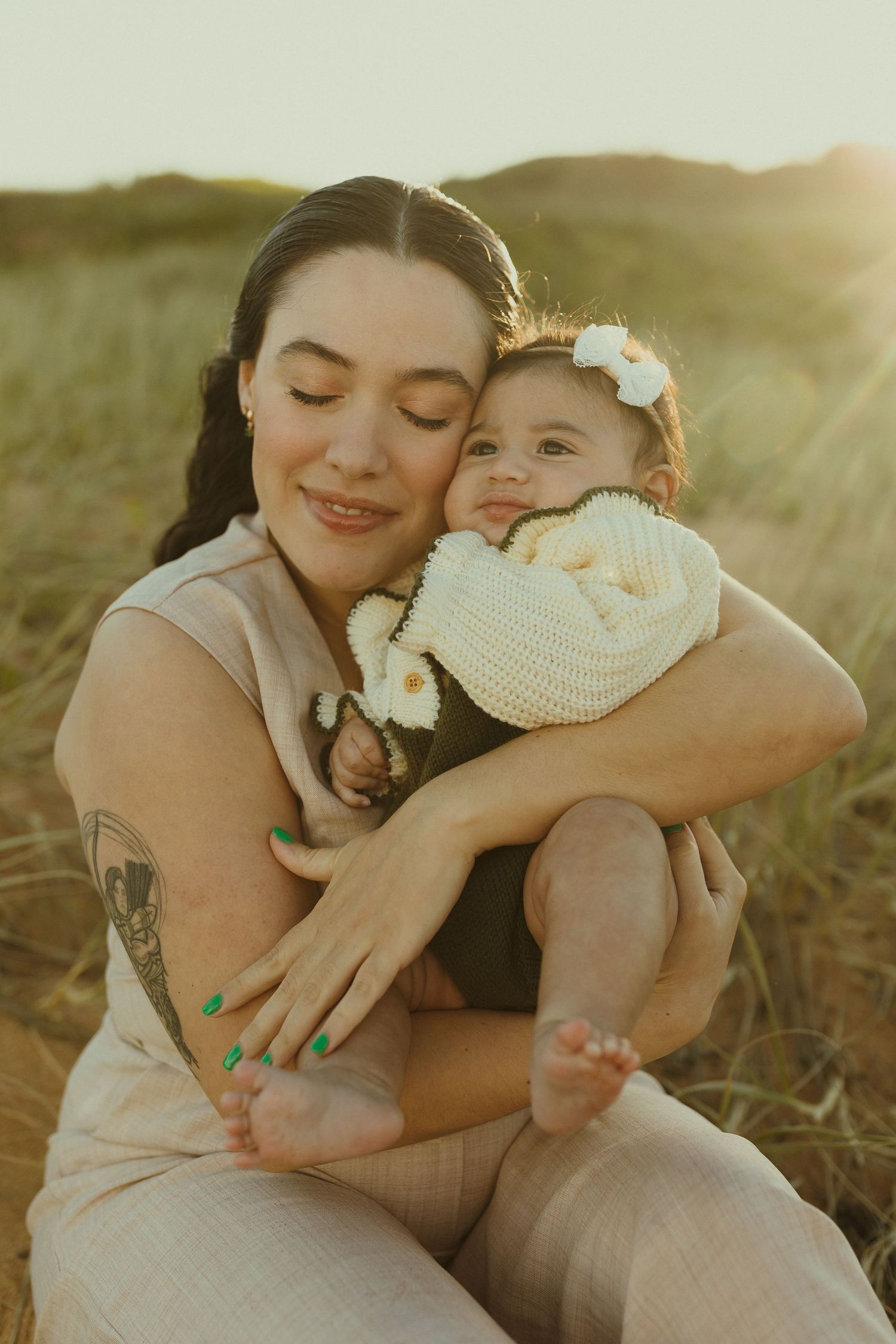 A tender loving moment between parent and baby in a sunlit field at golden hour.