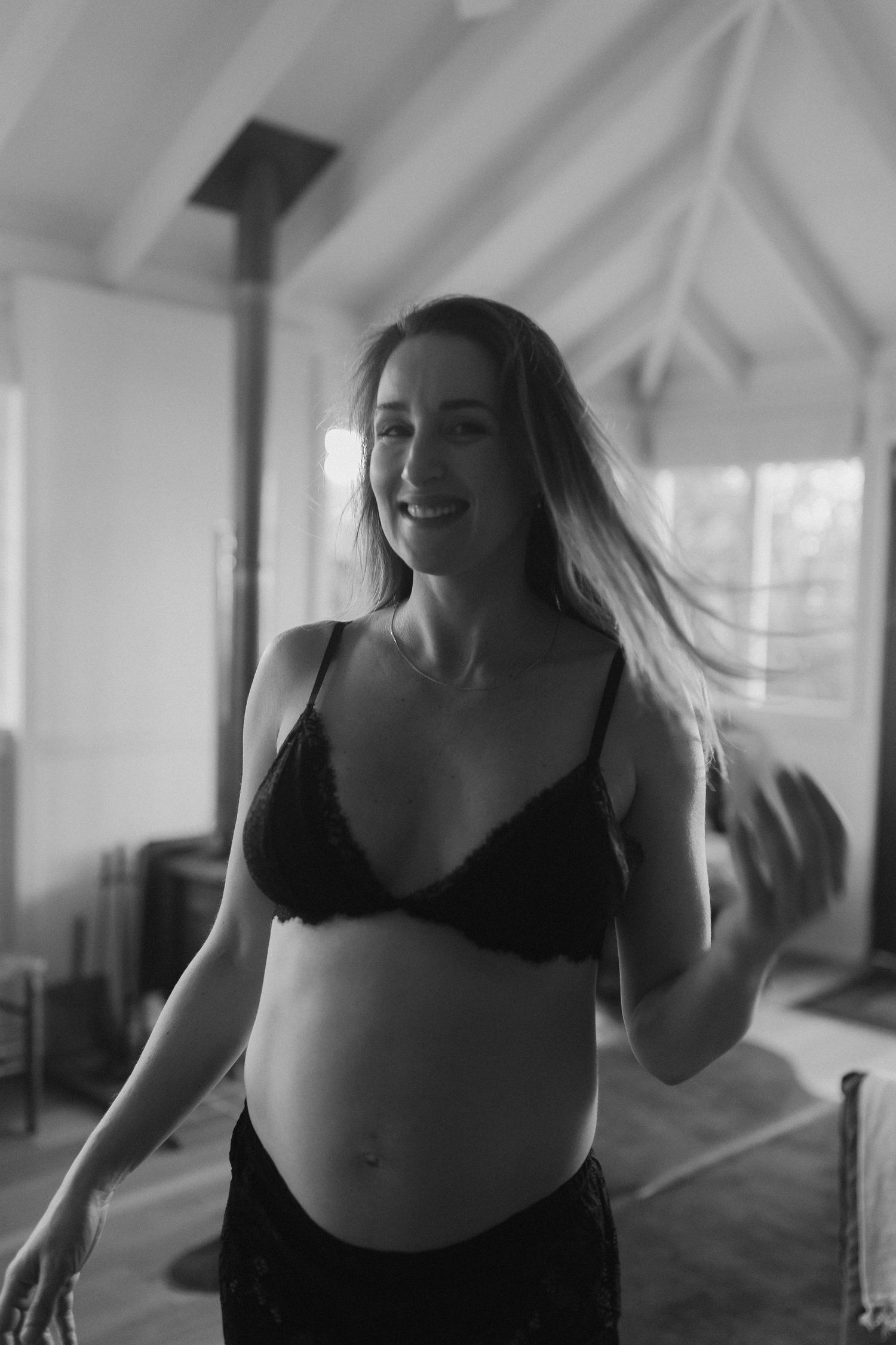 Black and white indoor maternity photo showing movement and joy in bright sunlit room.