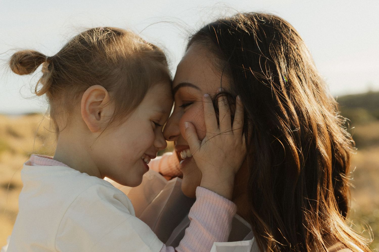 An intimate close-up moment between loved ones sharing affection outdoors in soft golden sunlight.