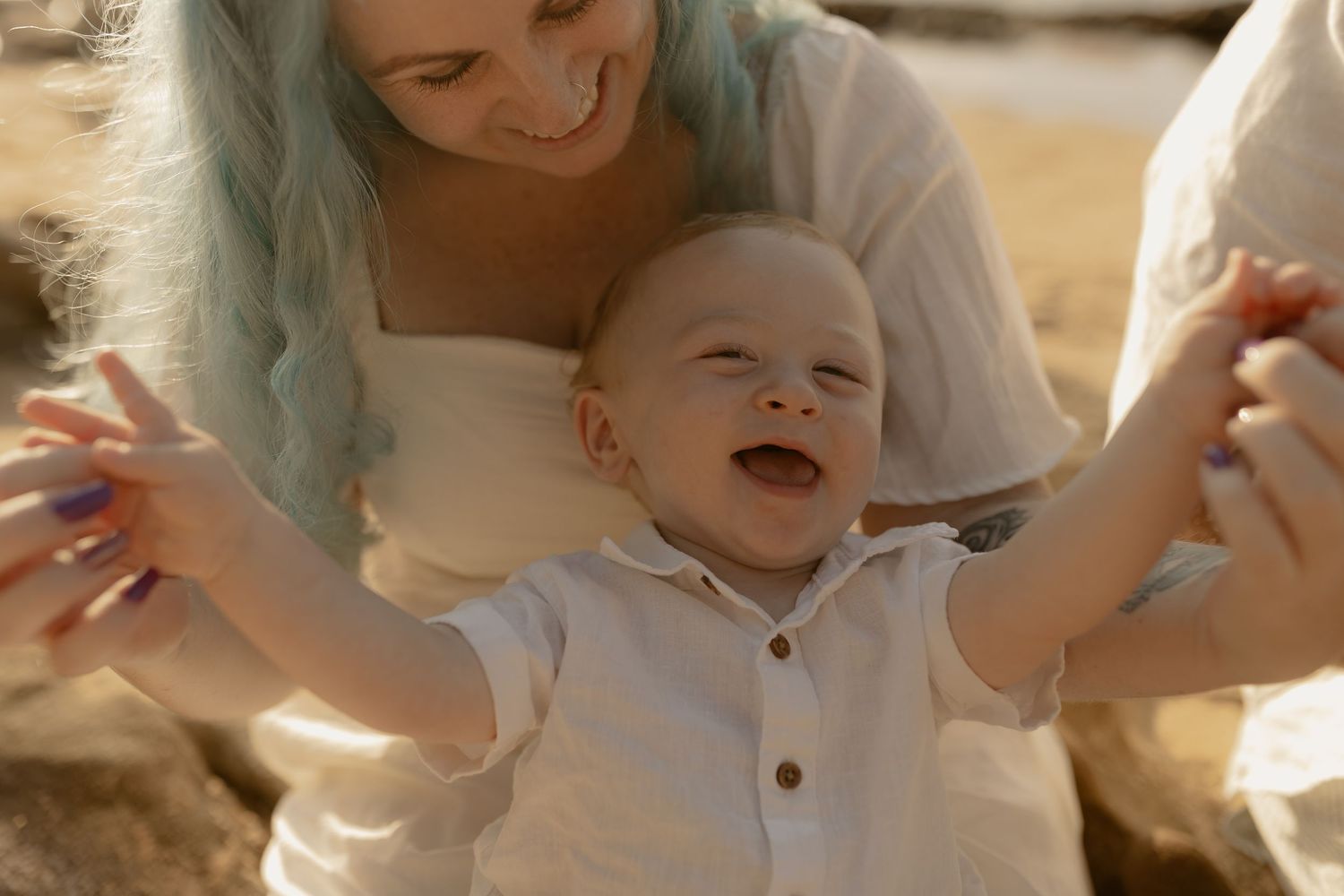 A baby laughs and plays while being held in someone's arms during a tender moment.