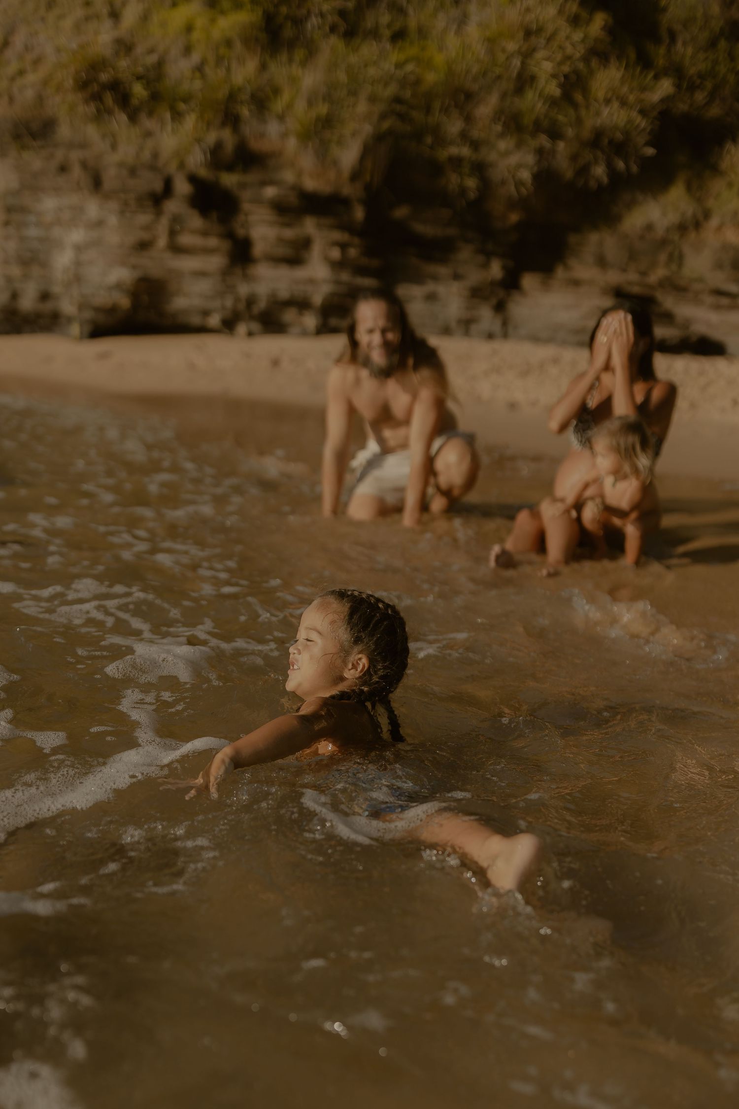 Children playing and splashing in shallow ocean waters during sunset.