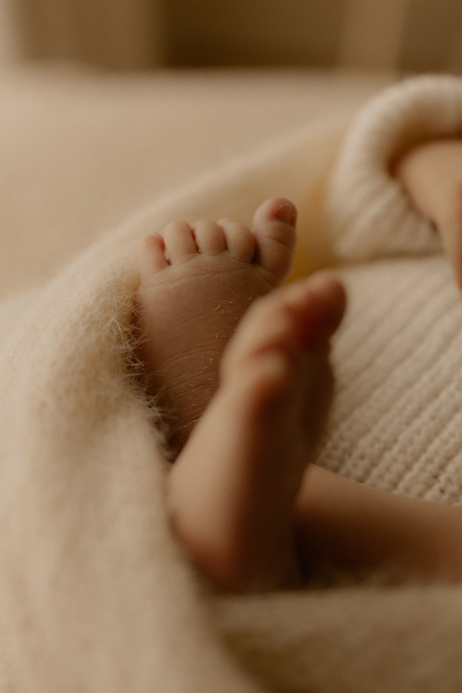 Close-up view of tiny baby feet resting on soft knitted fabric in warm sepia tones.
