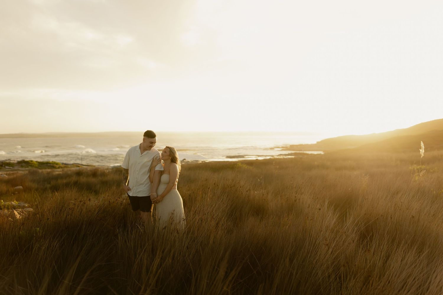 Silhouetted couple walking along coastal path during golden hour sunset.