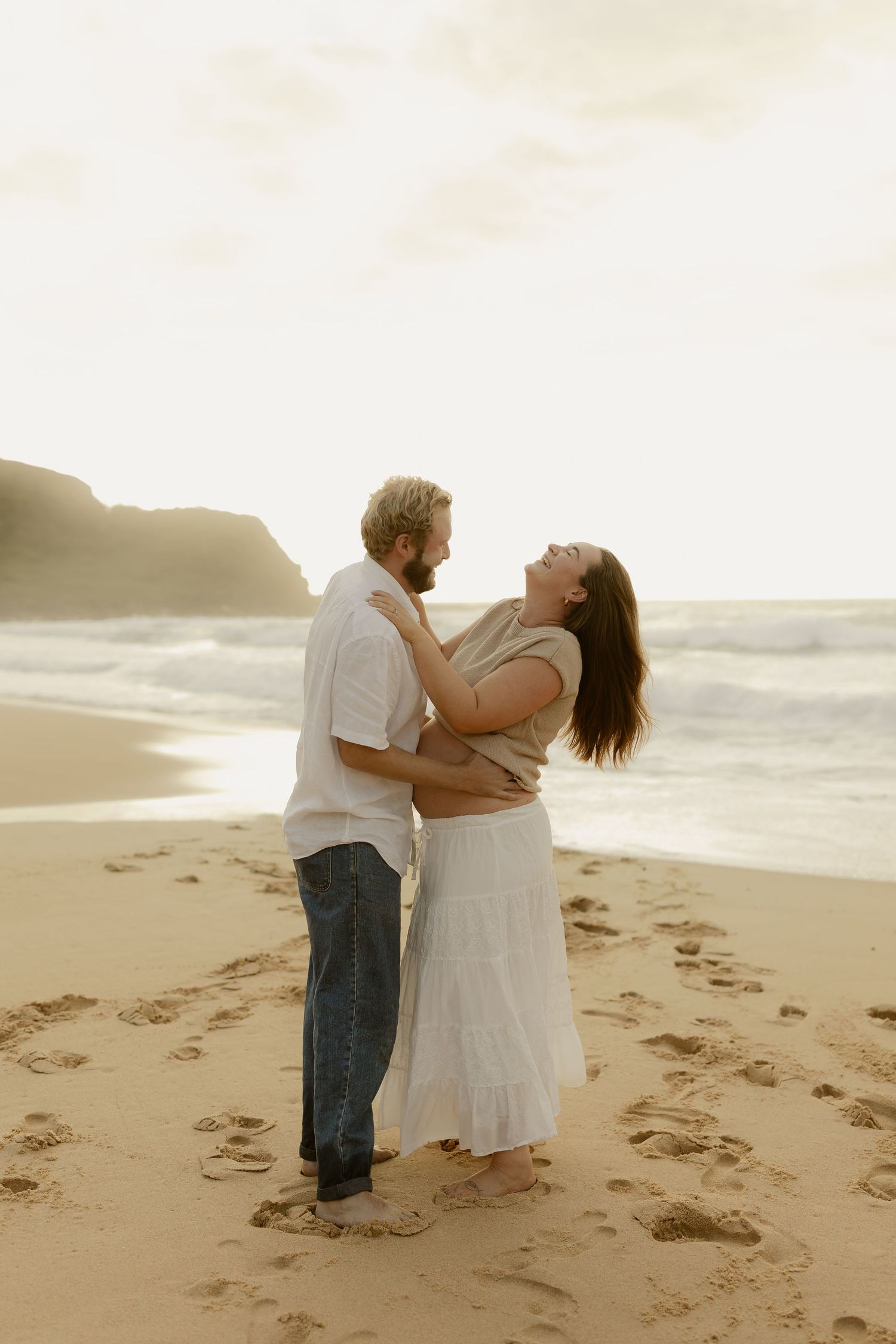 A couple shares intimate moments on a sandy beach during a golden hour photoshoot.