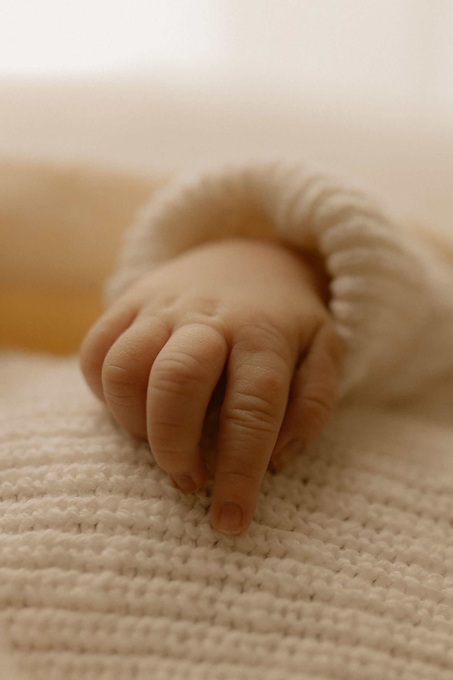 Close-up of a tiny baby's hand resting on a white knitted blanket in soft, warm lighting.