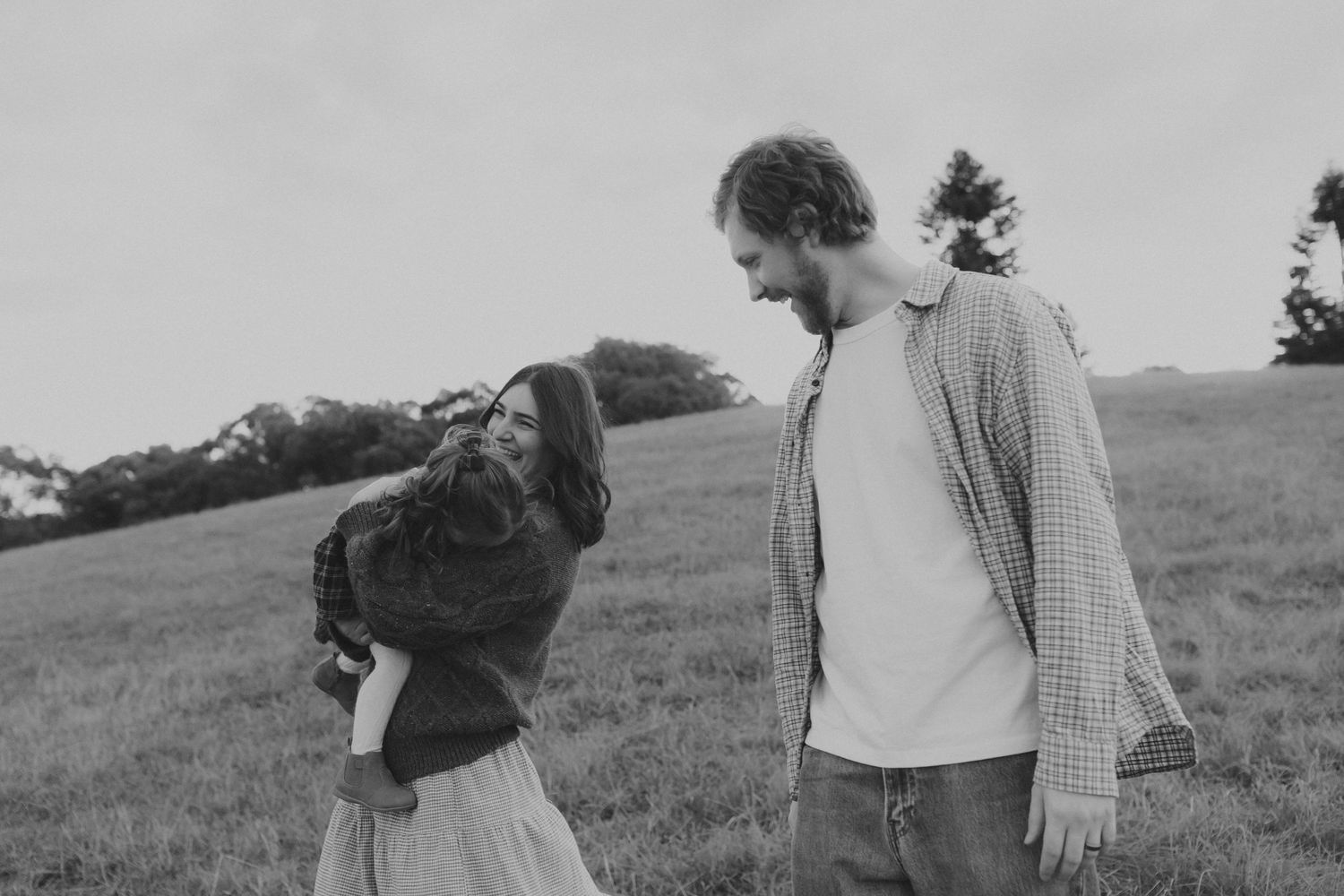 Black and white photo of a couple laughing together in a green field on a cloudy day.
