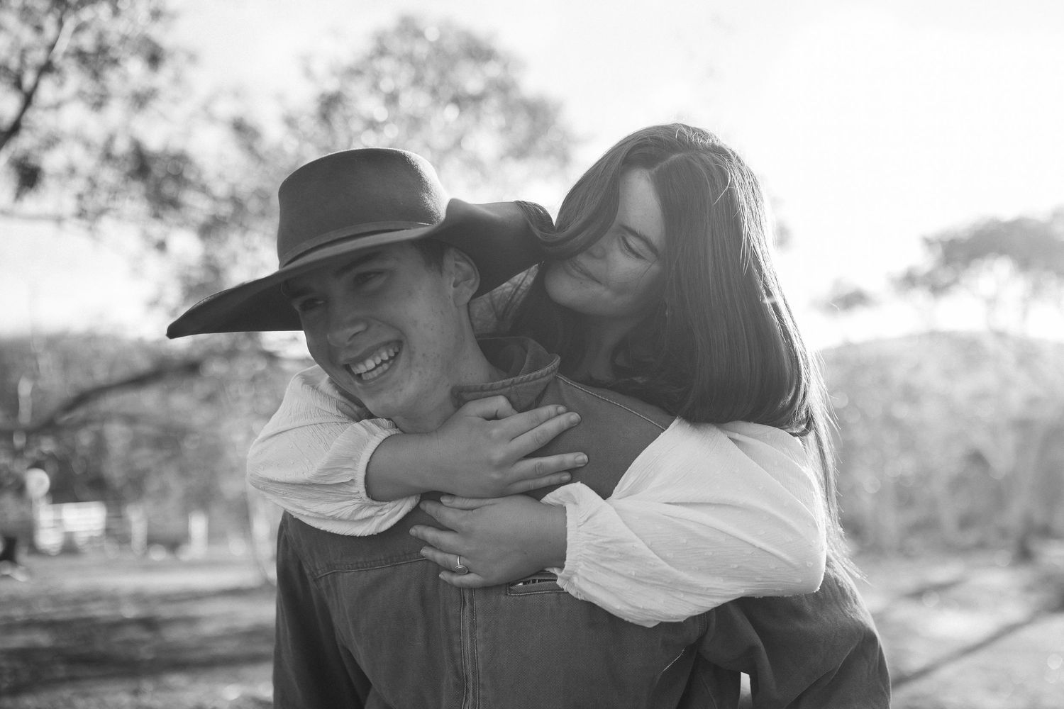 A playful black and white photo showing a couple embracing outdoors, with one wearing a cowboy hat.